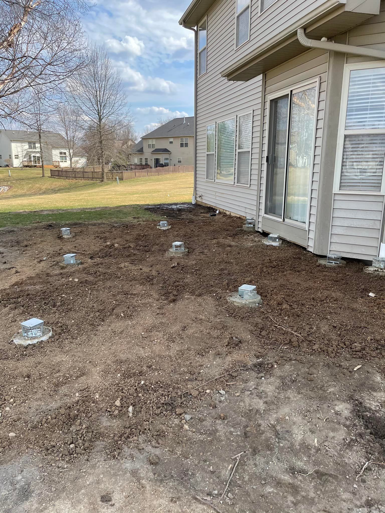 Dirt yard with concrete footings near a house, ready for construction.