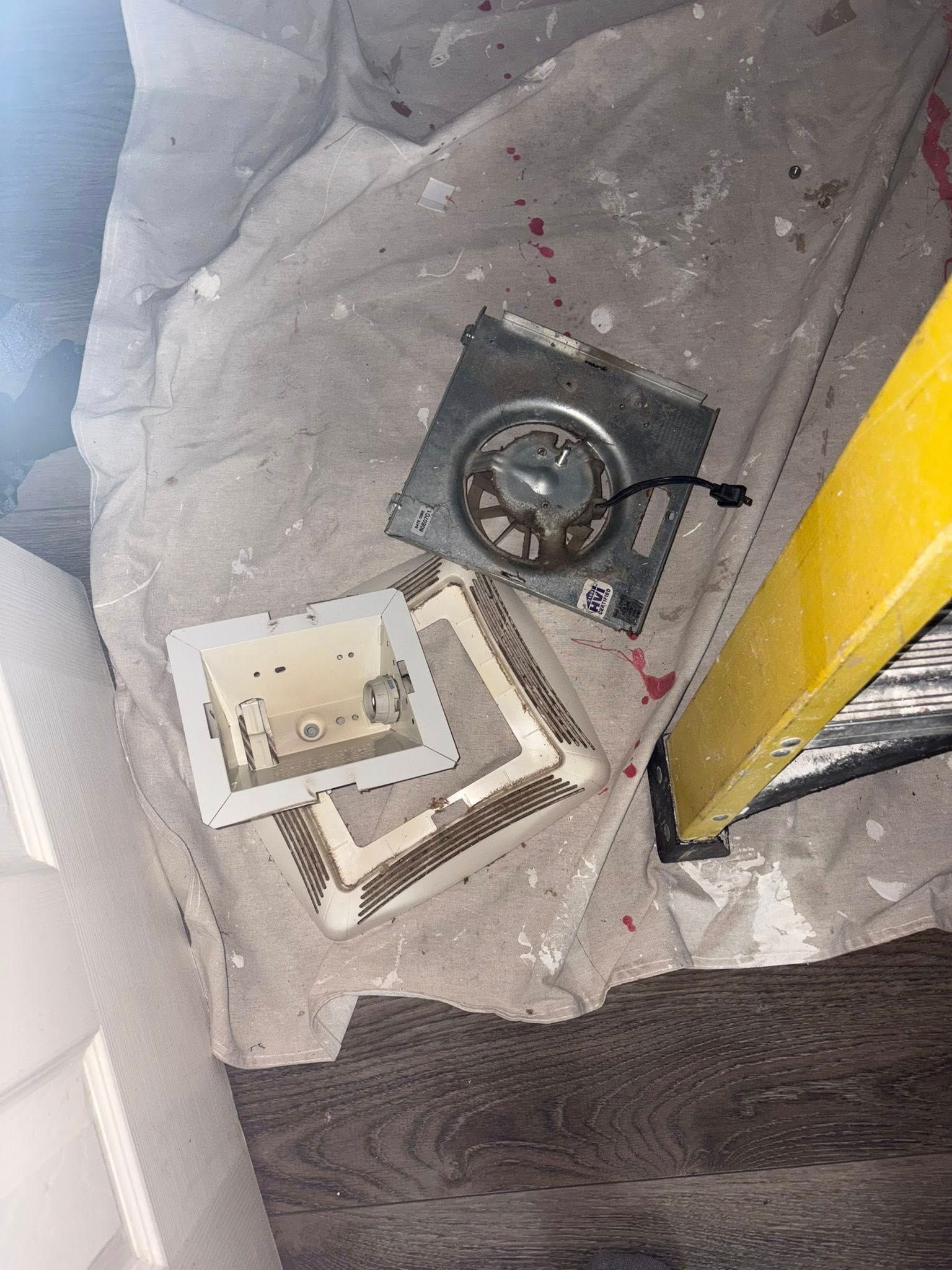 Parts of an air vent and a ladder on a drop cloth covered floor.