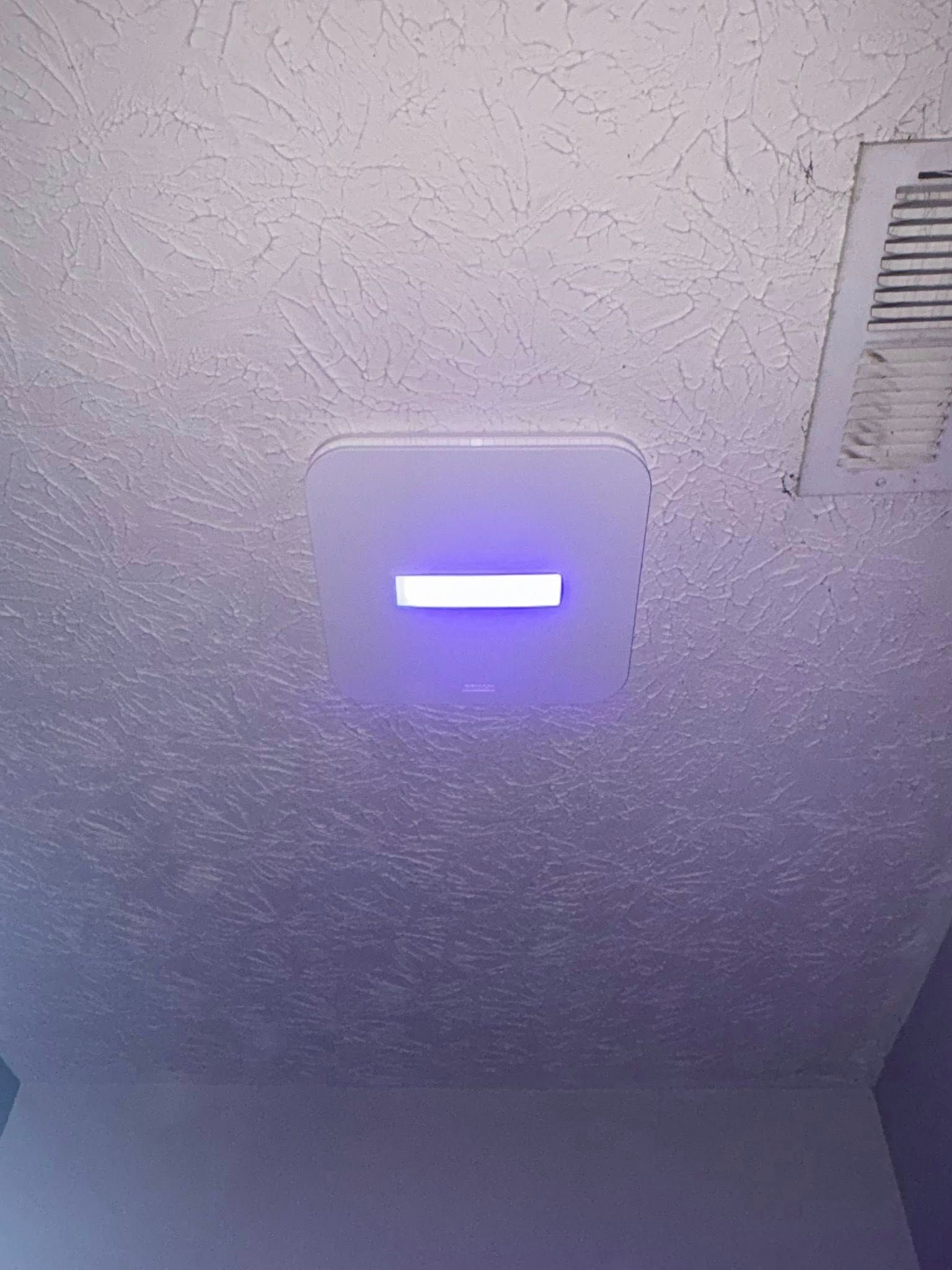 Ceiling with a rectangular light fixture emitting a horizontal white light and air vent.