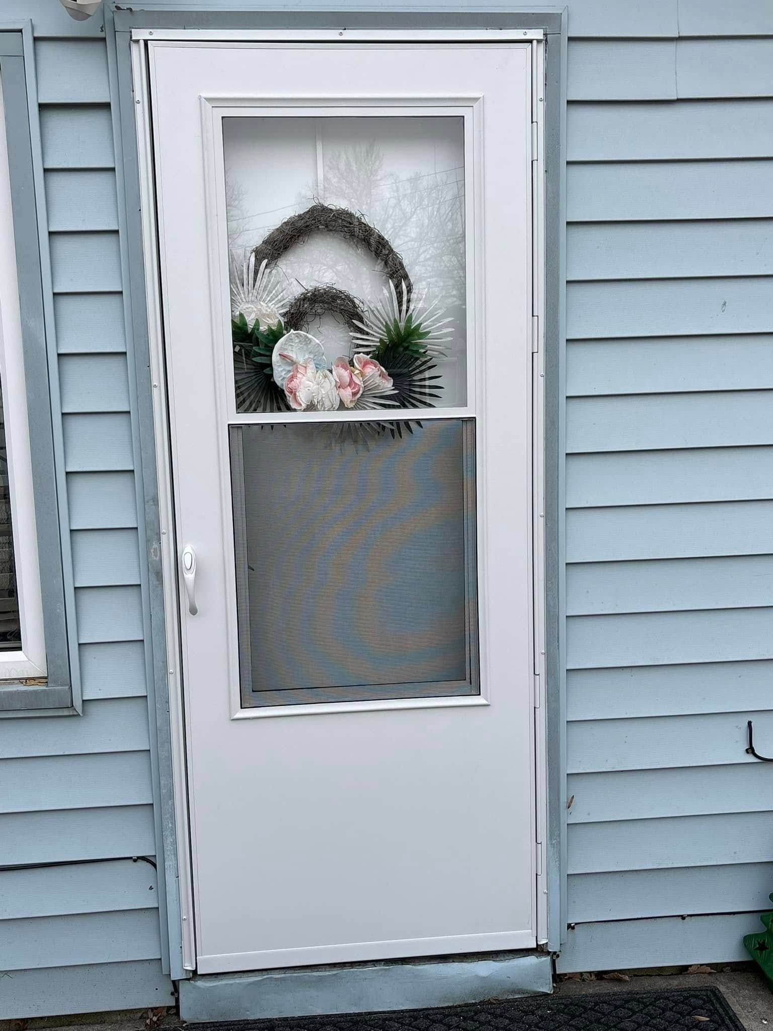 White door with a wreath hanging on it; blue siding on the wall.