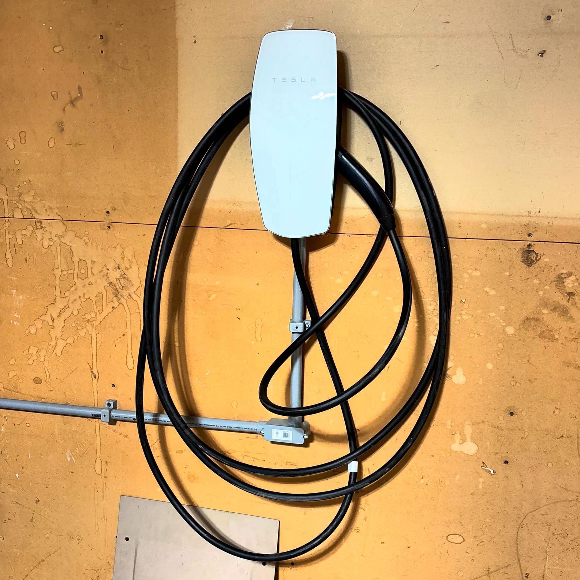Electric vehicle charger with black cable coiled on an orange-yellow wall.