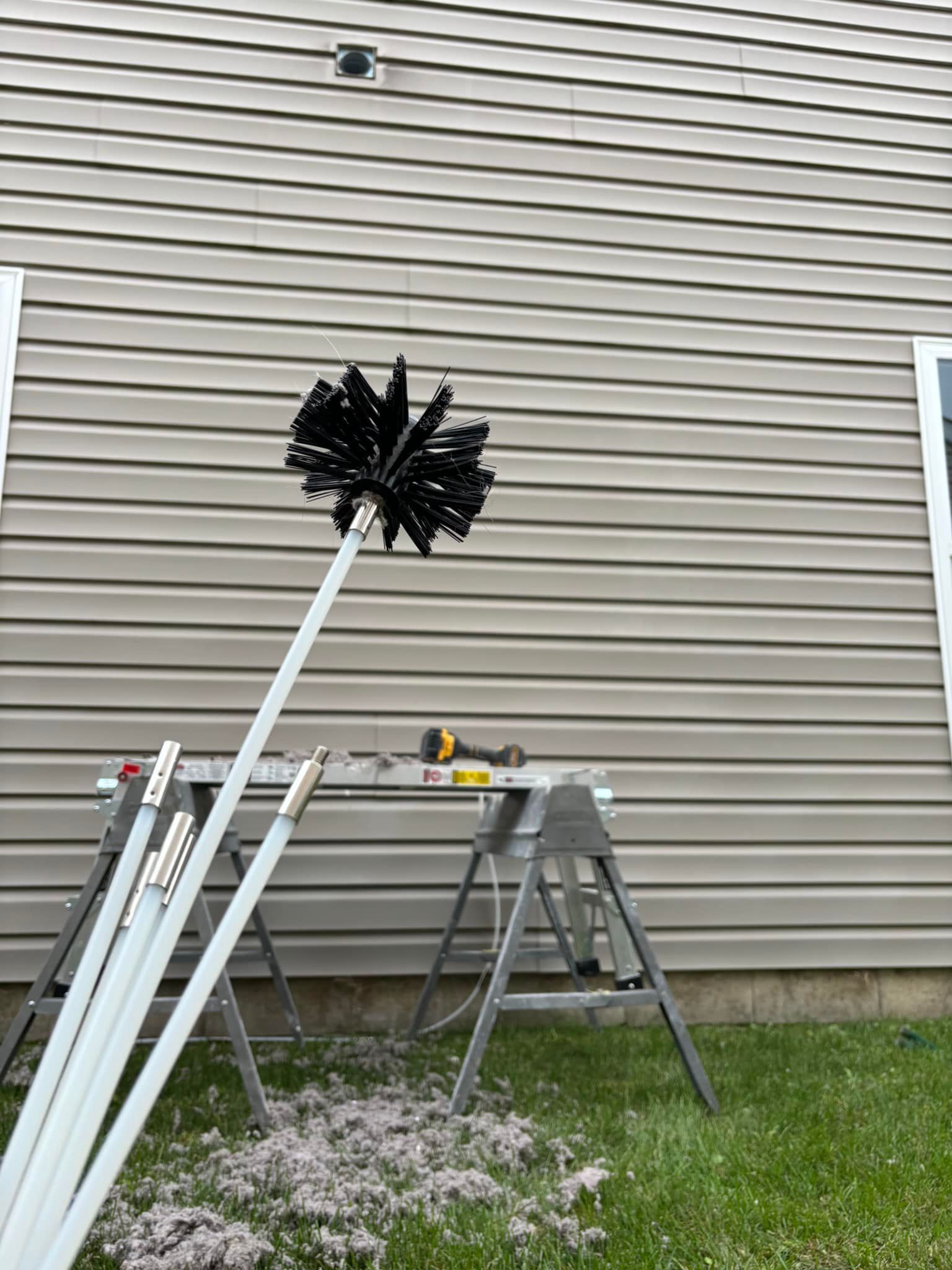 Chimney sweep tools with brush and poles set up outside, next to house with beige siding.