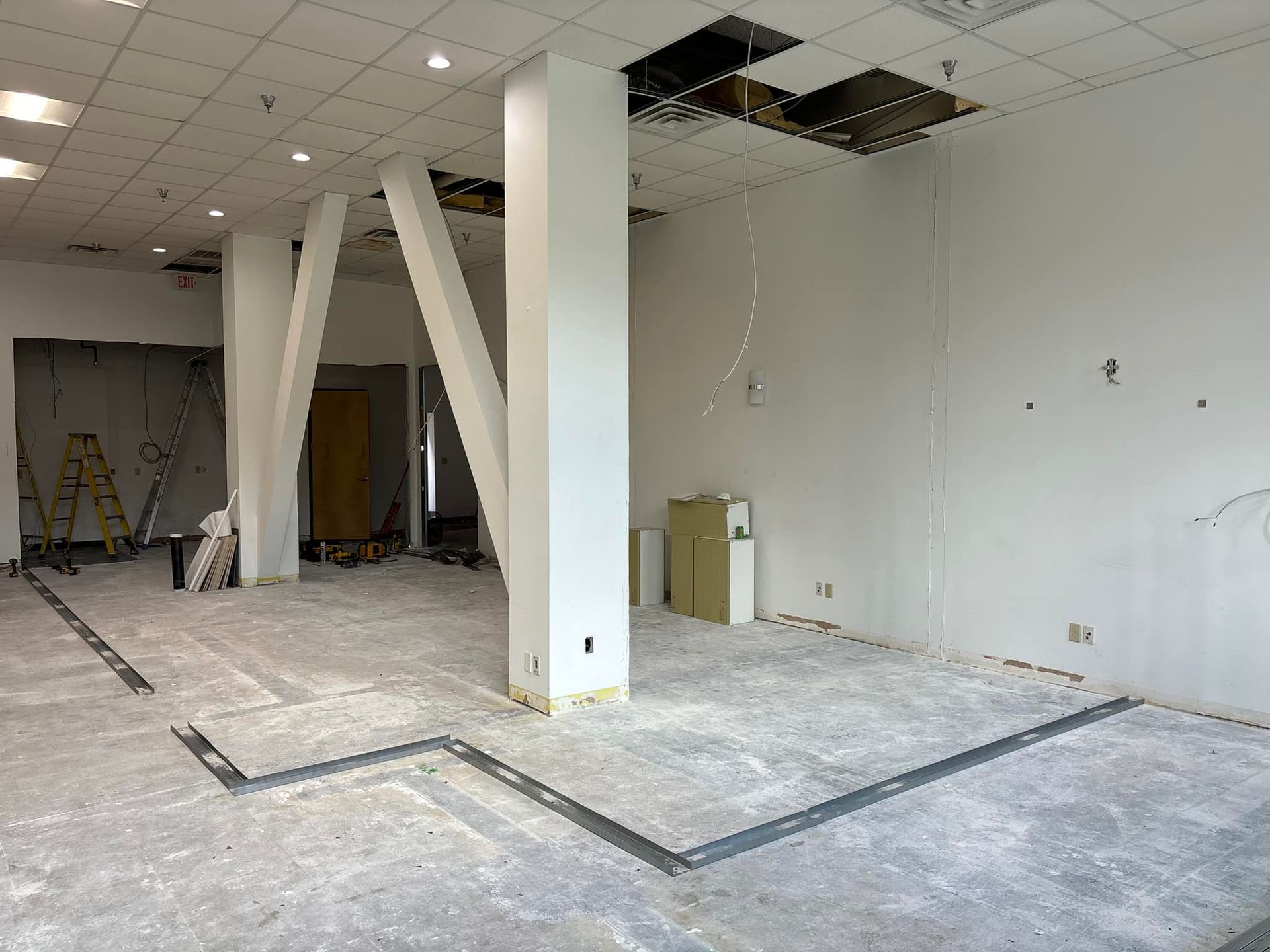 Interior of a room under construction with support beams, exposed ceiling, and concrete floor.