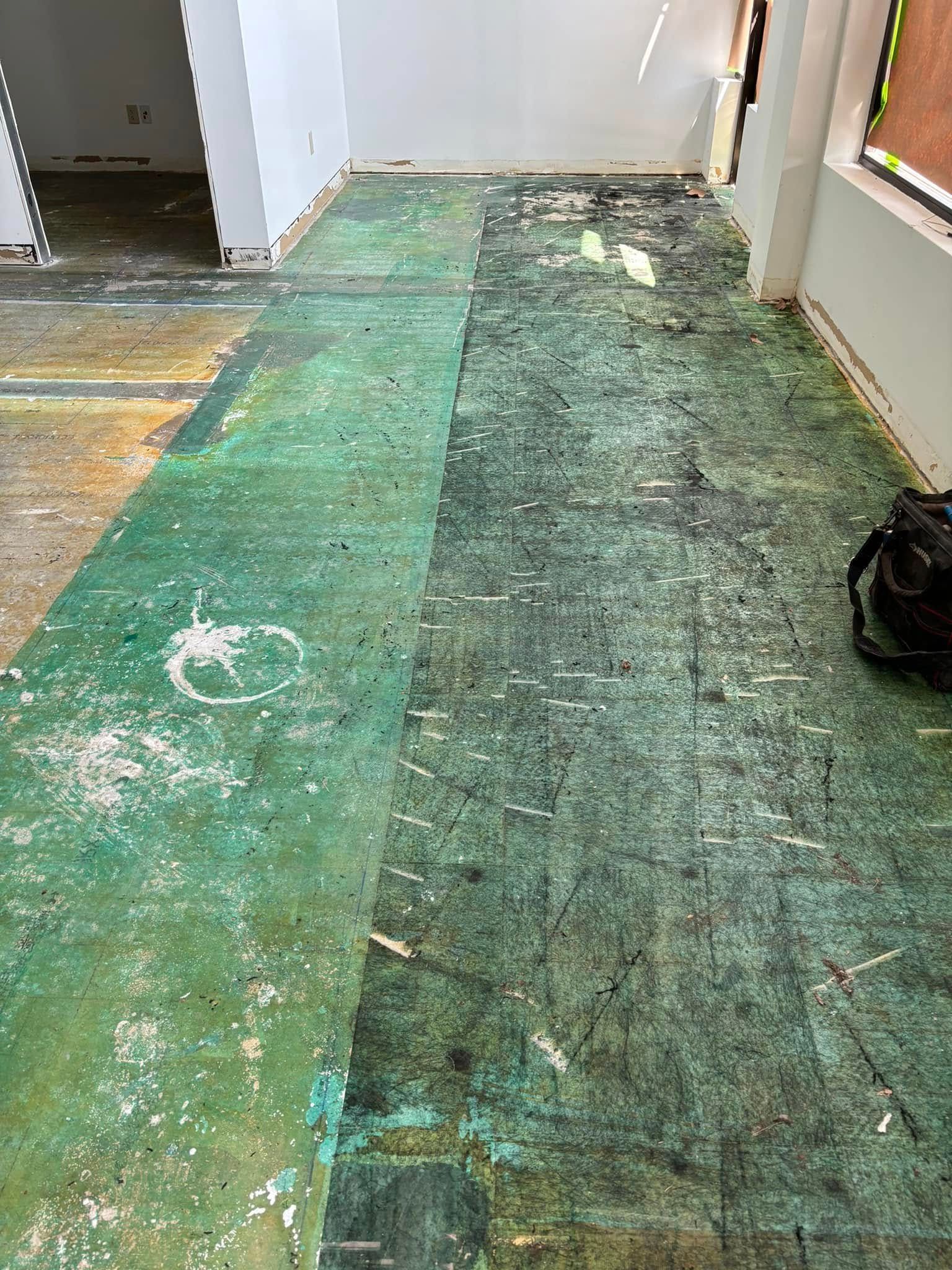 Green and black flooring during renovation, showing damage and debris.