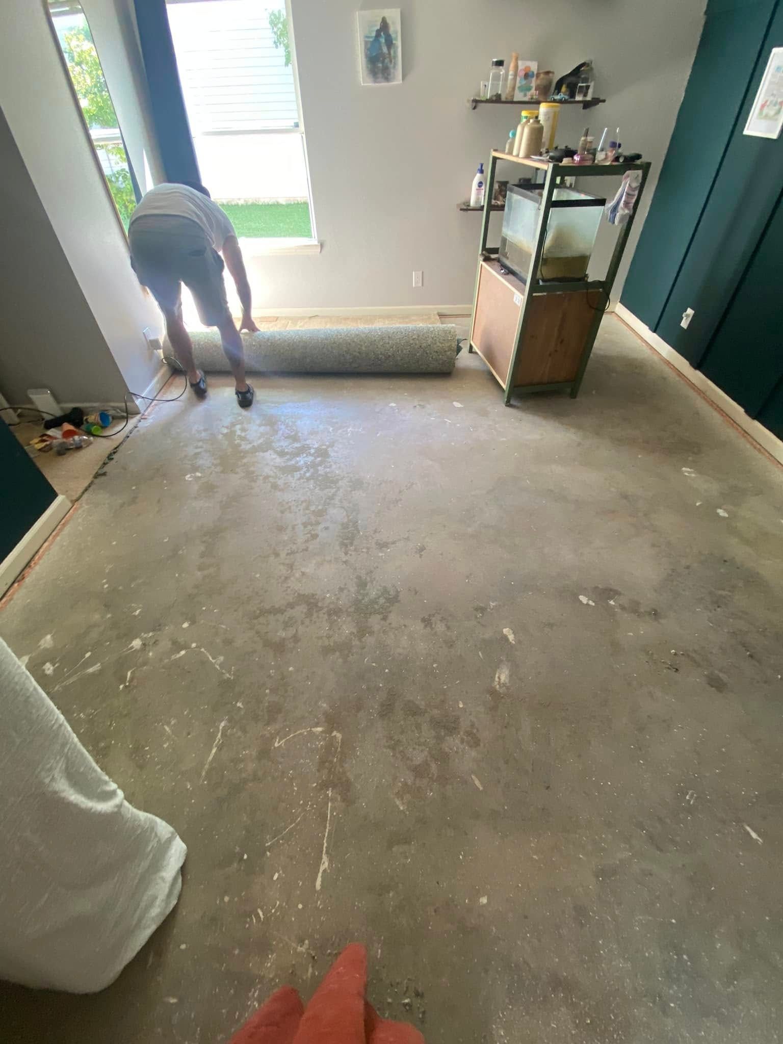 Person rolling out a carpet in a room with concrete floors, near a window and an aquarium.