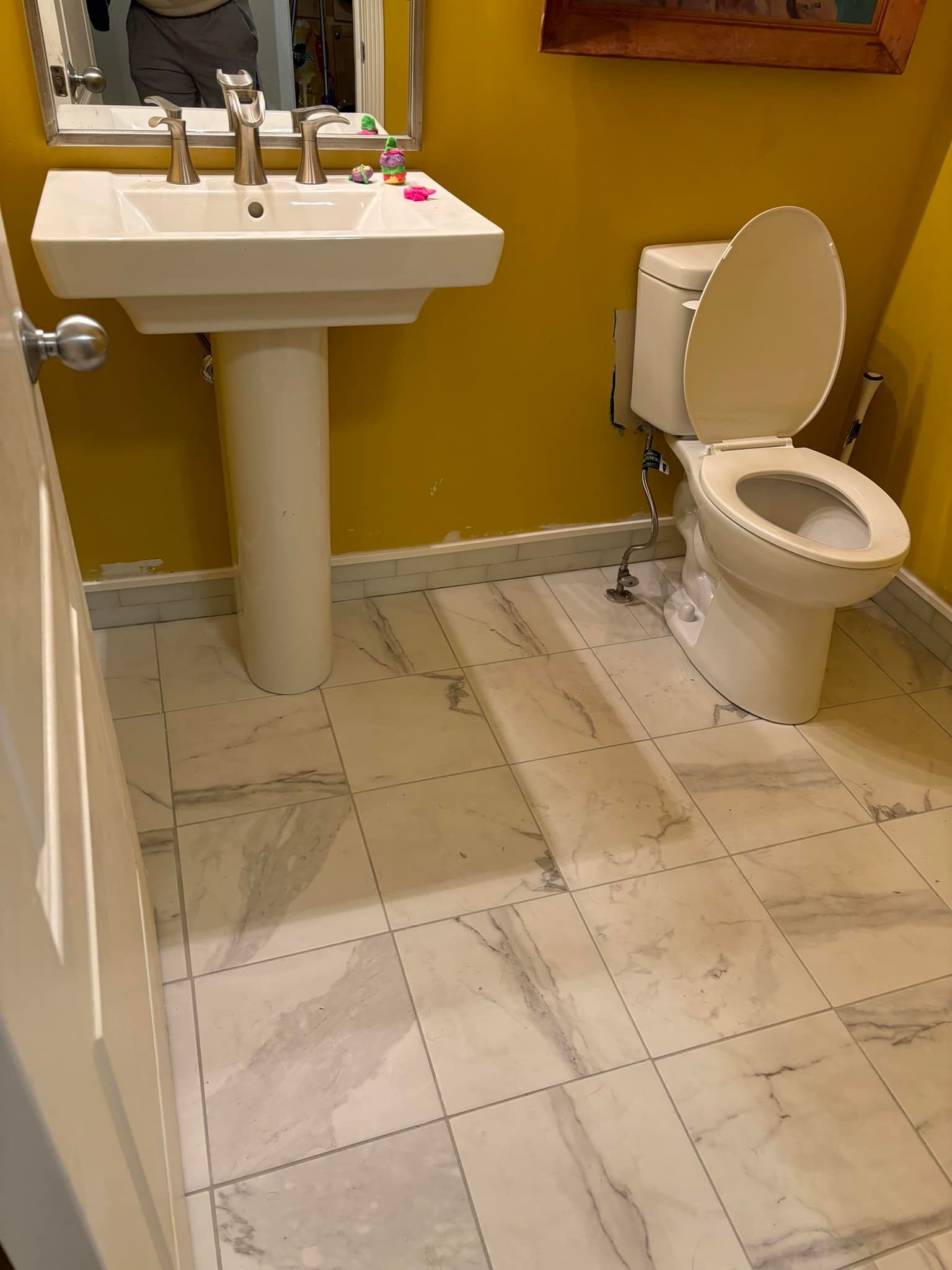 Bathroom with a white pedestal sink and toilet on marble-patterned floors, yellow walls.