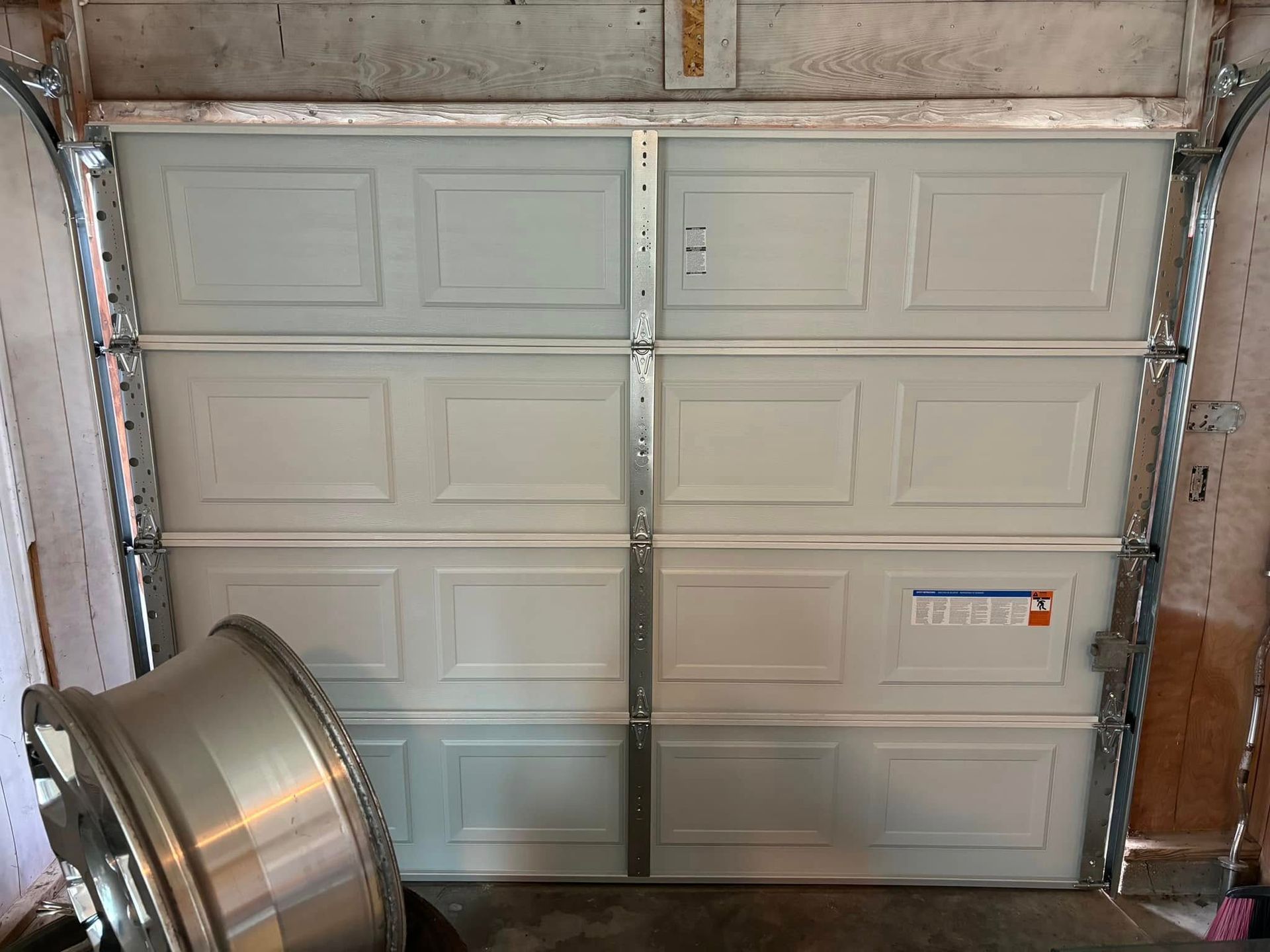White garage door, partially open, with a car wheel in the foreground.