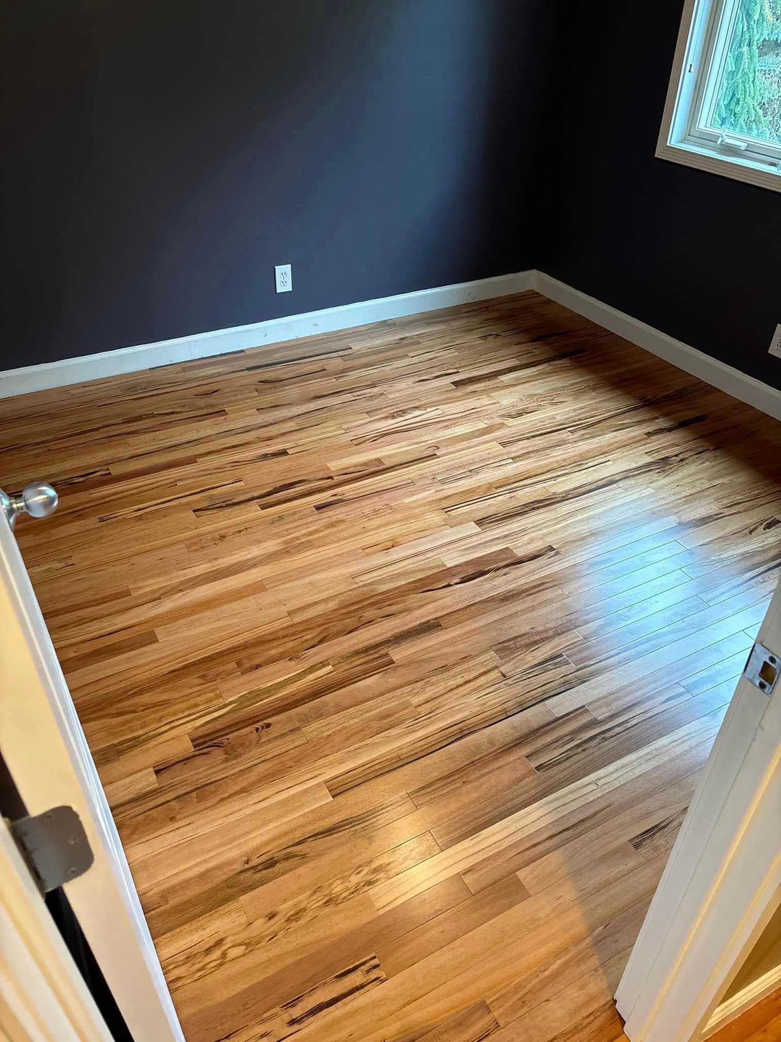 Hardwood floor in a room with dark purple walls and a small window.