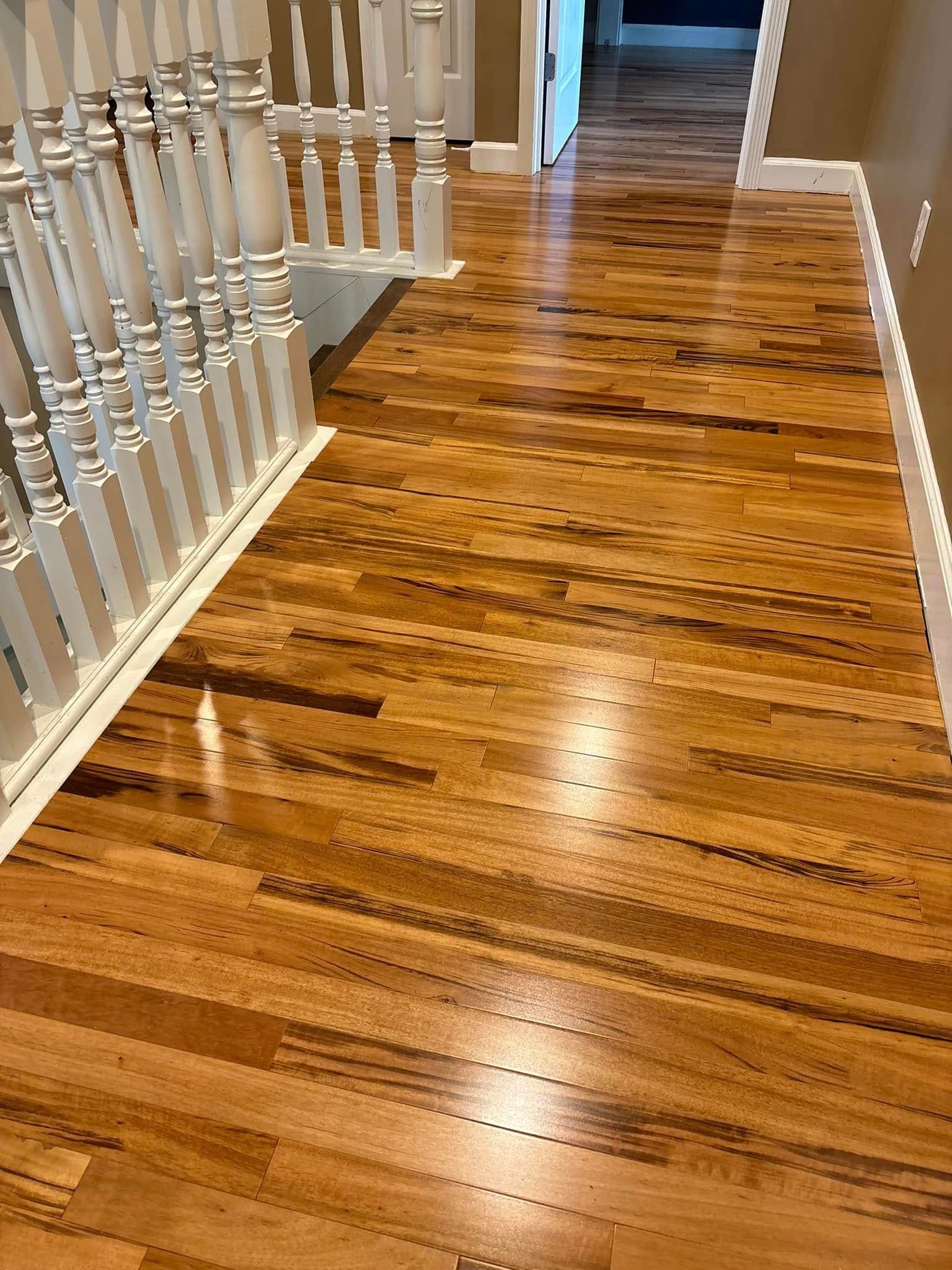Hardwood floors in a hallway with a white railing. The wood has brown and tan hues.