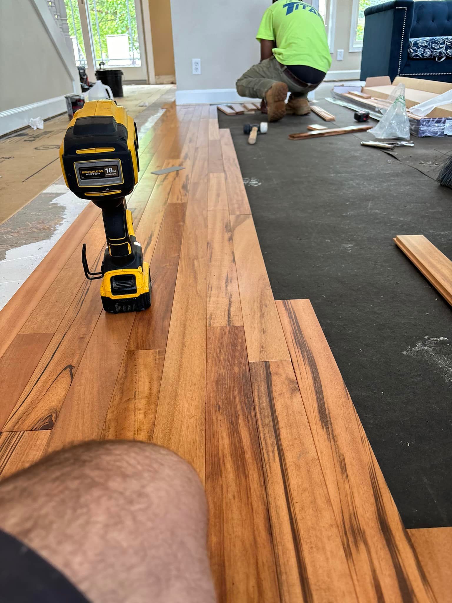 Person installing hardwood floors with a nail gun; close-up of flooring.