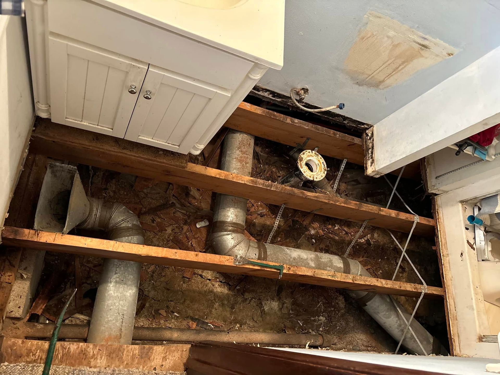 View from below of kitchen cabinet and exposed floor joists with ductwork and debris visible.