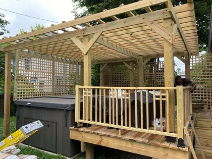Wooden pergola over a hot tub on a deck, with latticework and railings, outdoors.