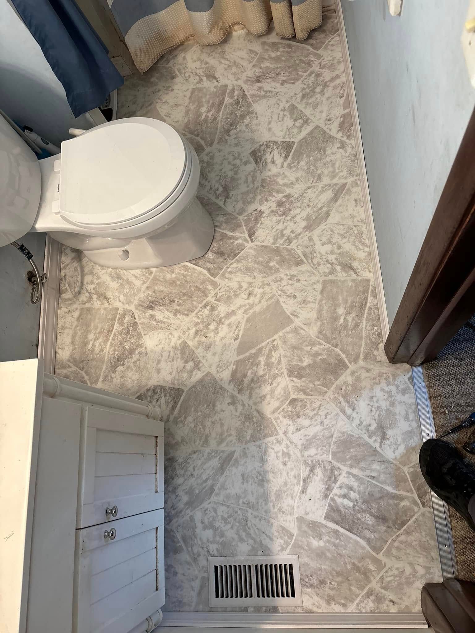 Bathroom floor with gray patterned tile; toilet, vanity, and heating vent visible.
