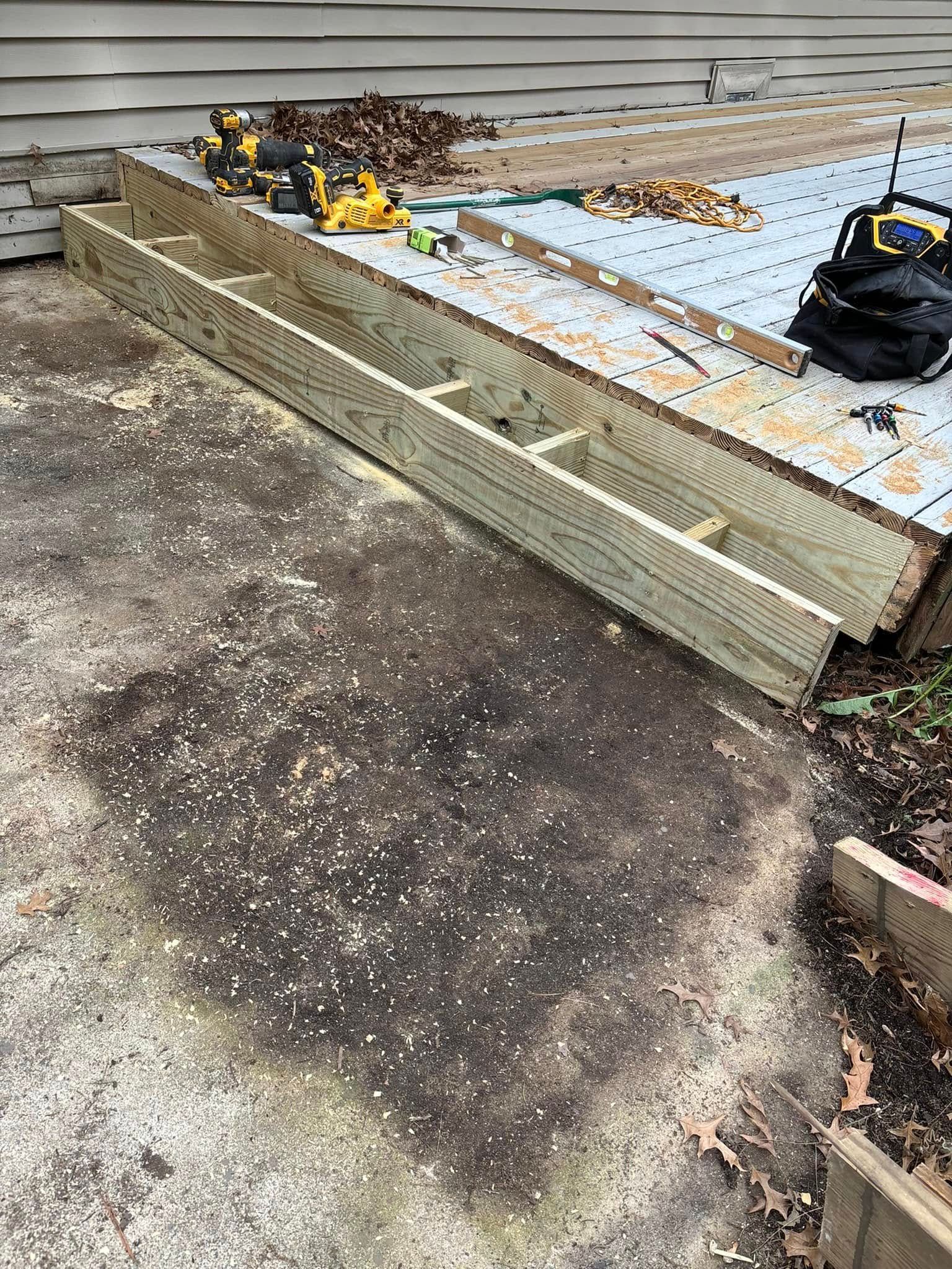 Wooden deck frame laid on a stained concrete patio next to a building. Tools and debris are visible.