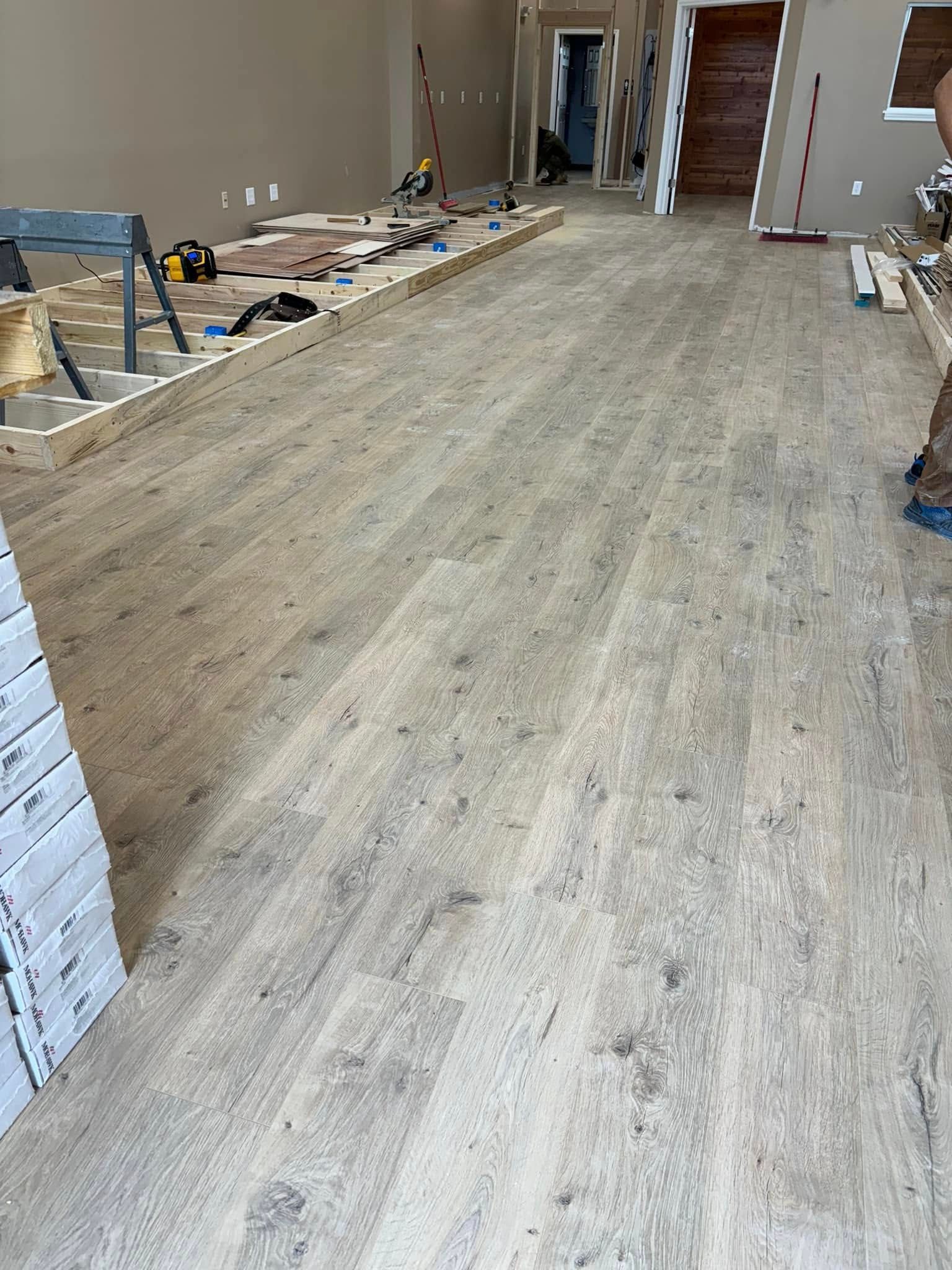 Light wood-look flooring installed in a room under construction. Tools and materials visible.