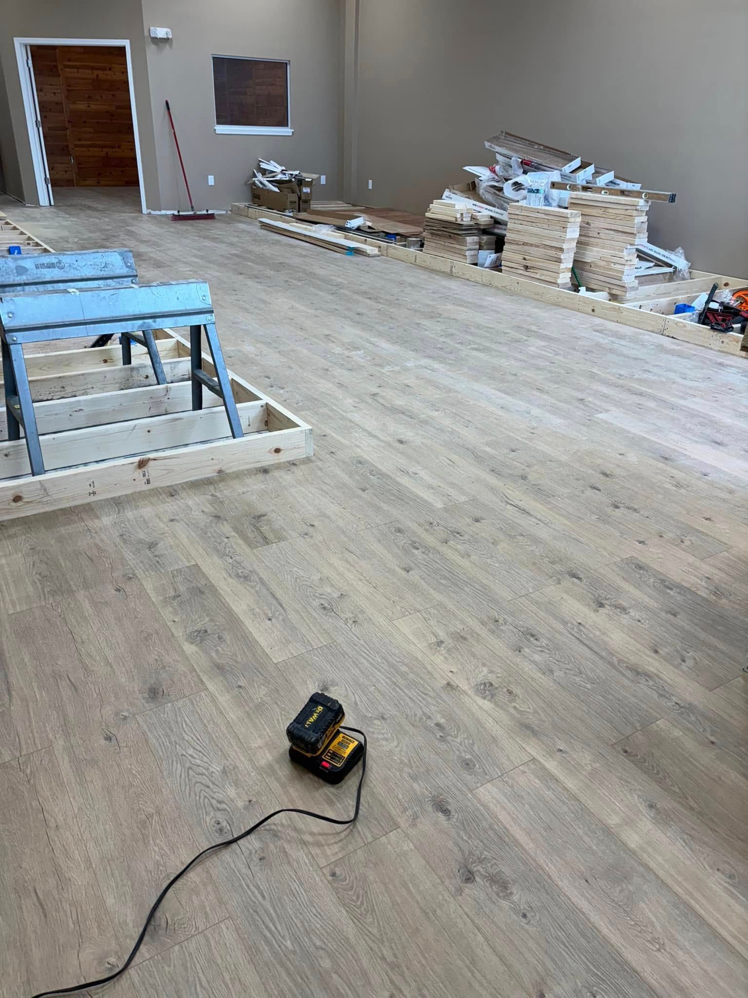 Wood flooring under construction with tools, sawhorses, and materials in a large room.