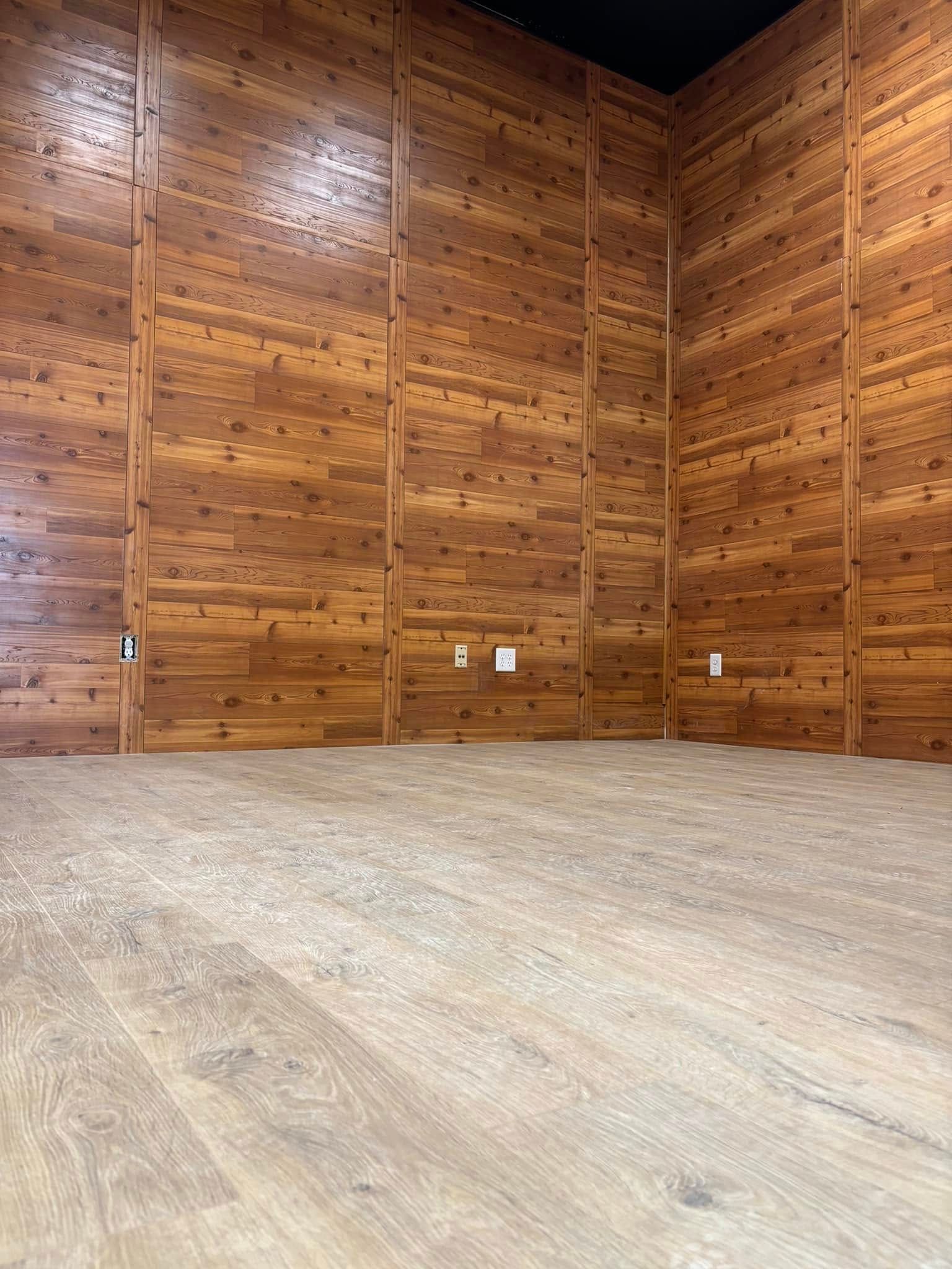 Empty room with wooden walls, wood-look flooring, and a black ceiling.