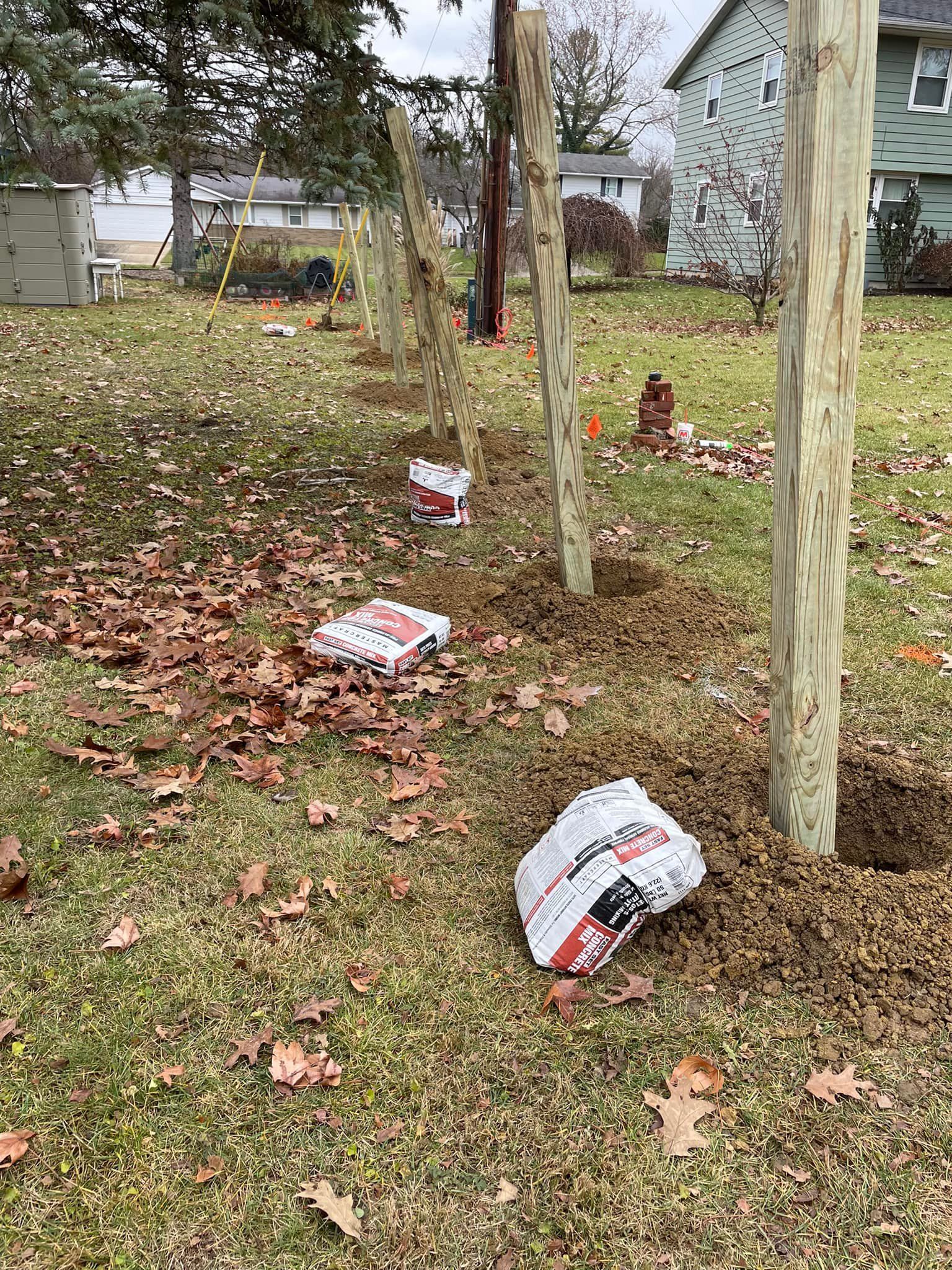 Fence posts being installed in a grassy yard; bags of cement are placed around the posts.