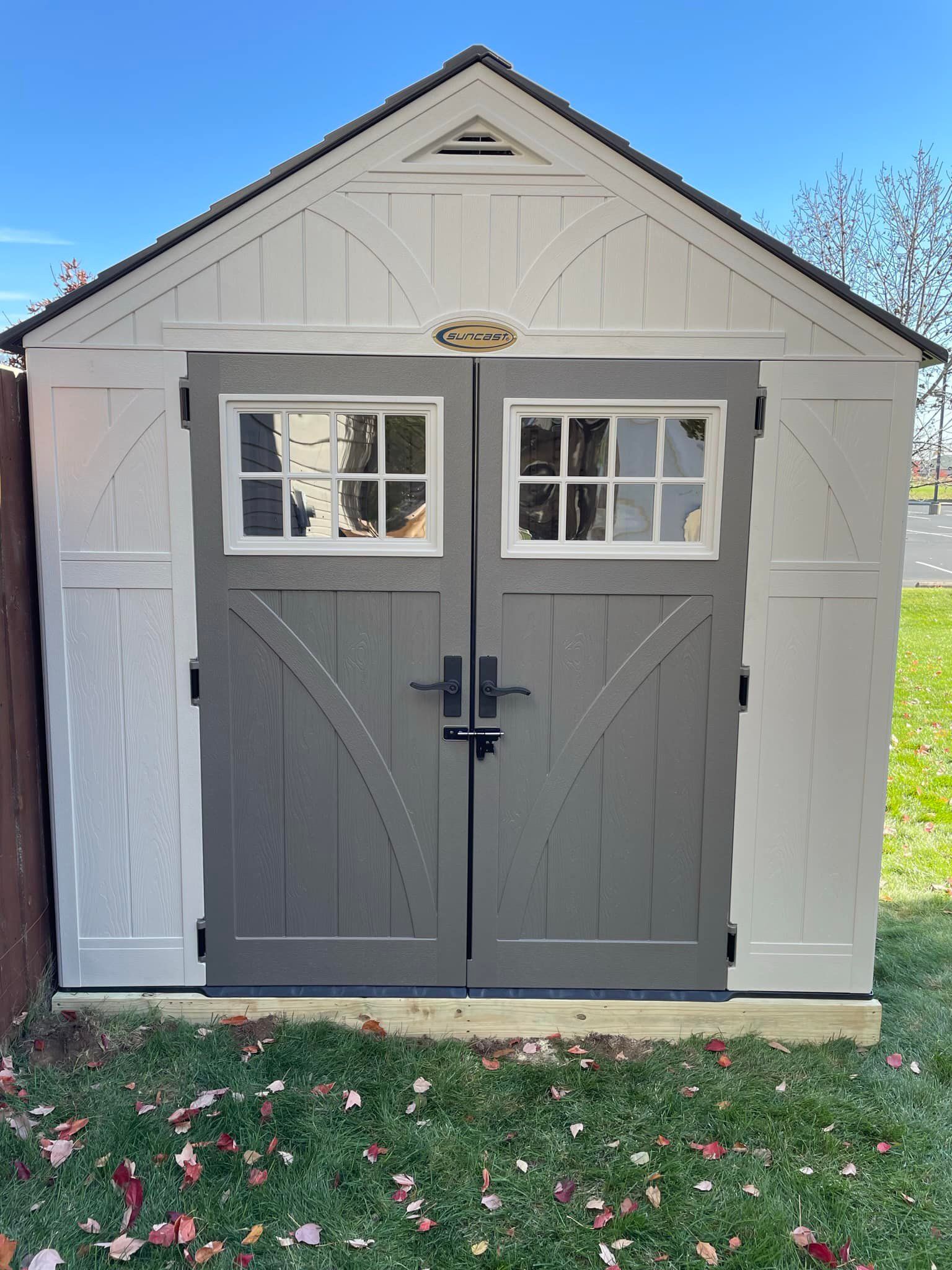 Gray shed with double doors, white frame, windows, and black hardware, set on a grassy lawn.