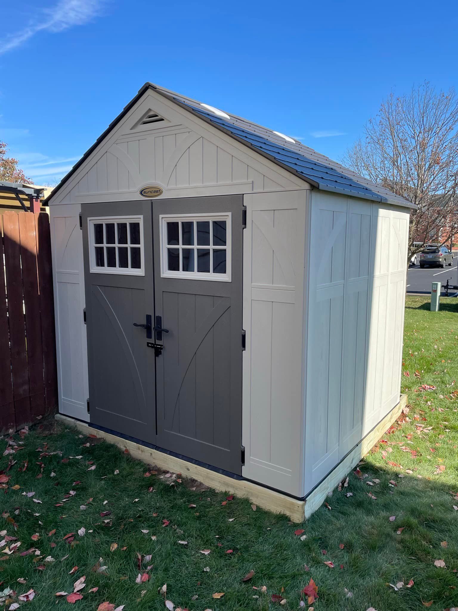 Gray and white outdoor storage shed with double doors, windows, and black roof.
