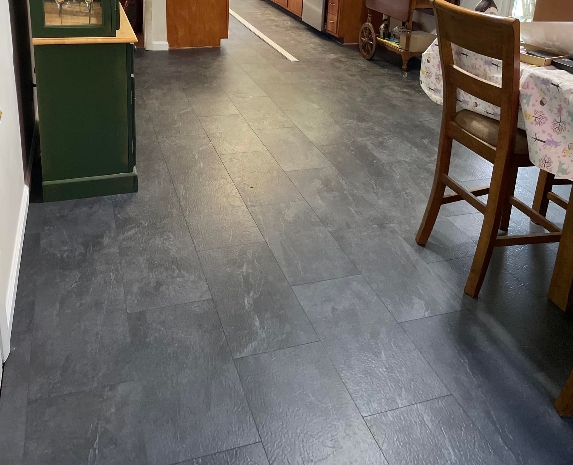 Dark gray tile flooring in a kitchen, with a green cabinet and a wooden chair and table visible.