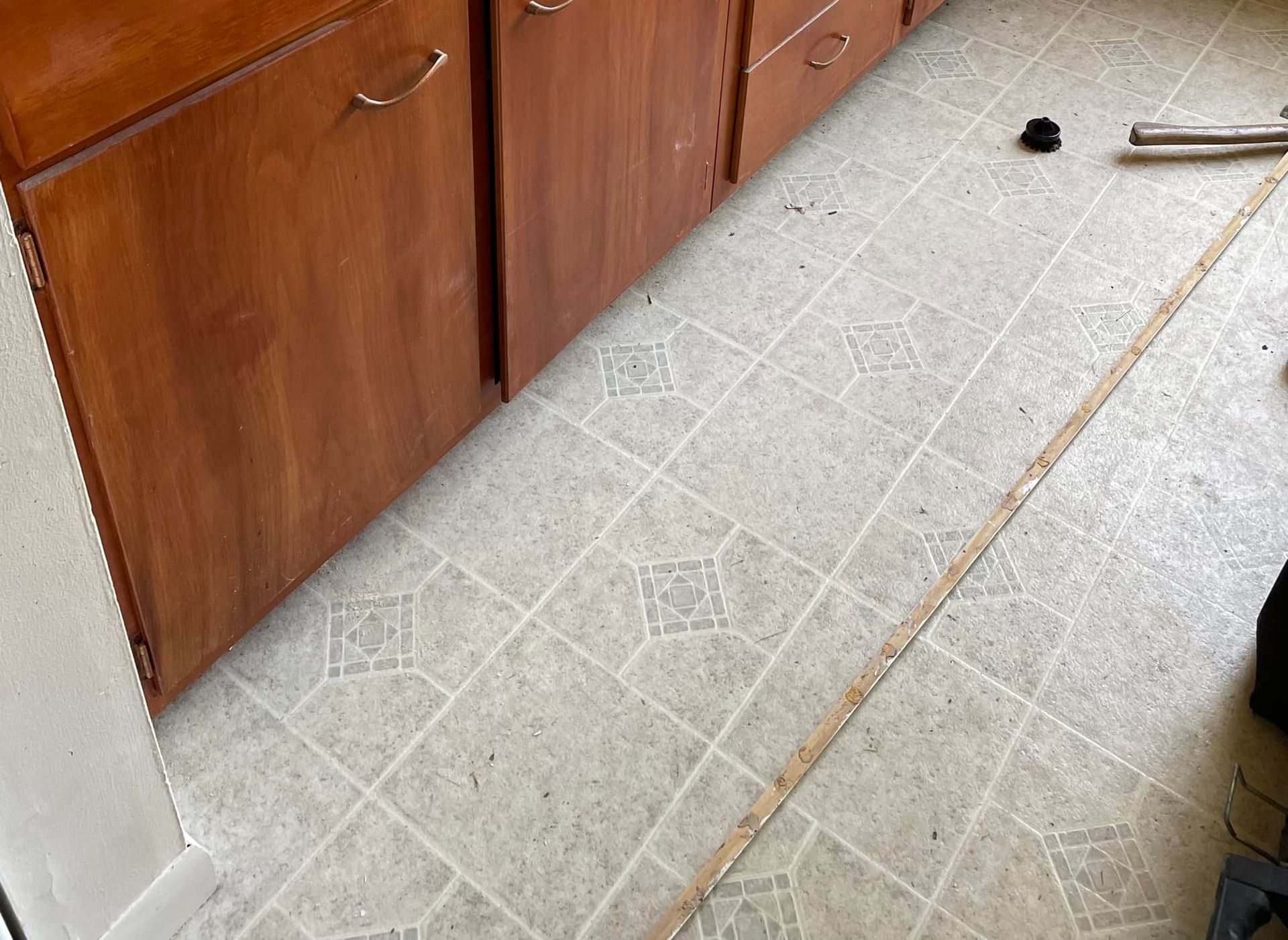 Wooden cabinets and light-colored tiled floor in a kitchen; measuring tape laid out.