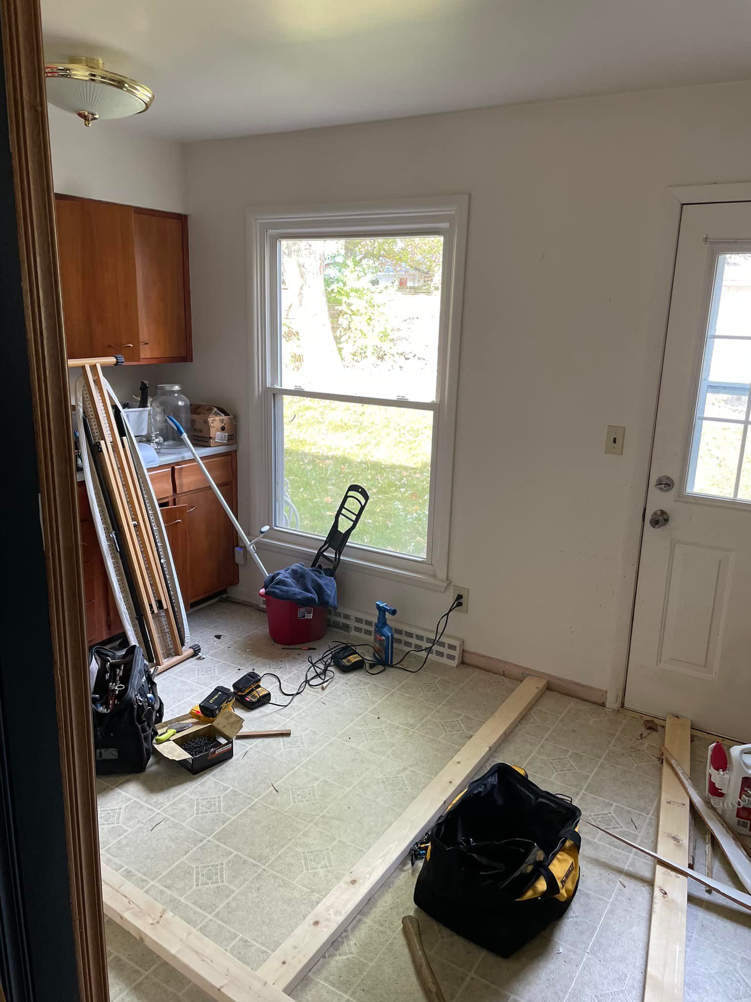 Kitchen remodel in progress: tools, wood, and debris on the floor, with a window and door visible.