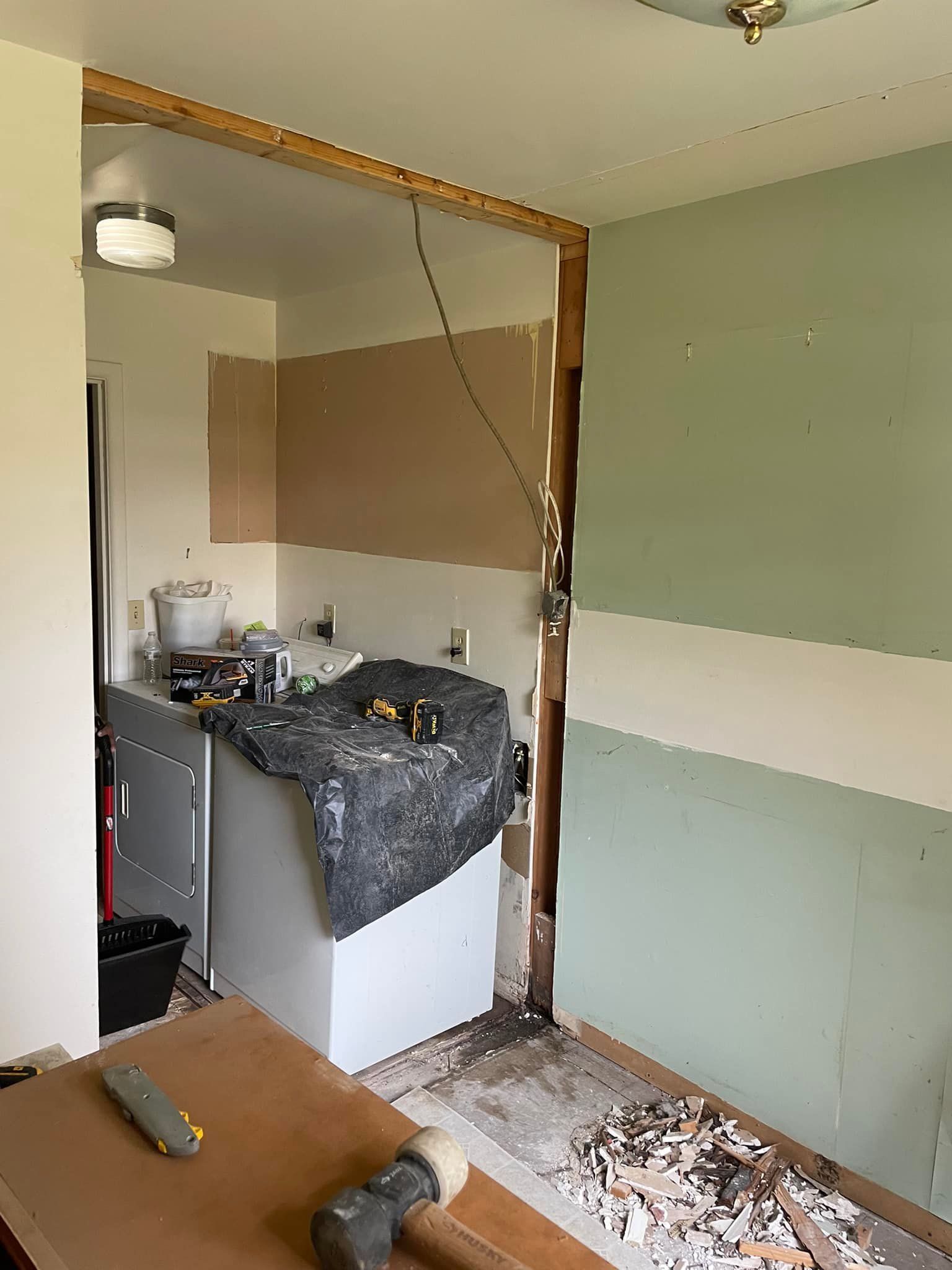Kitchen renovation in progress. Exposed studs, partially removed wall, cabinet, tools, and debris.