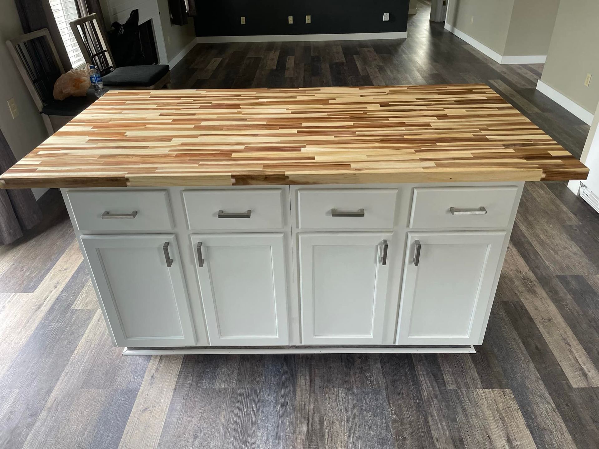 Kitchen island with a wood countertop and white cabinets, on wood-look flooring.
