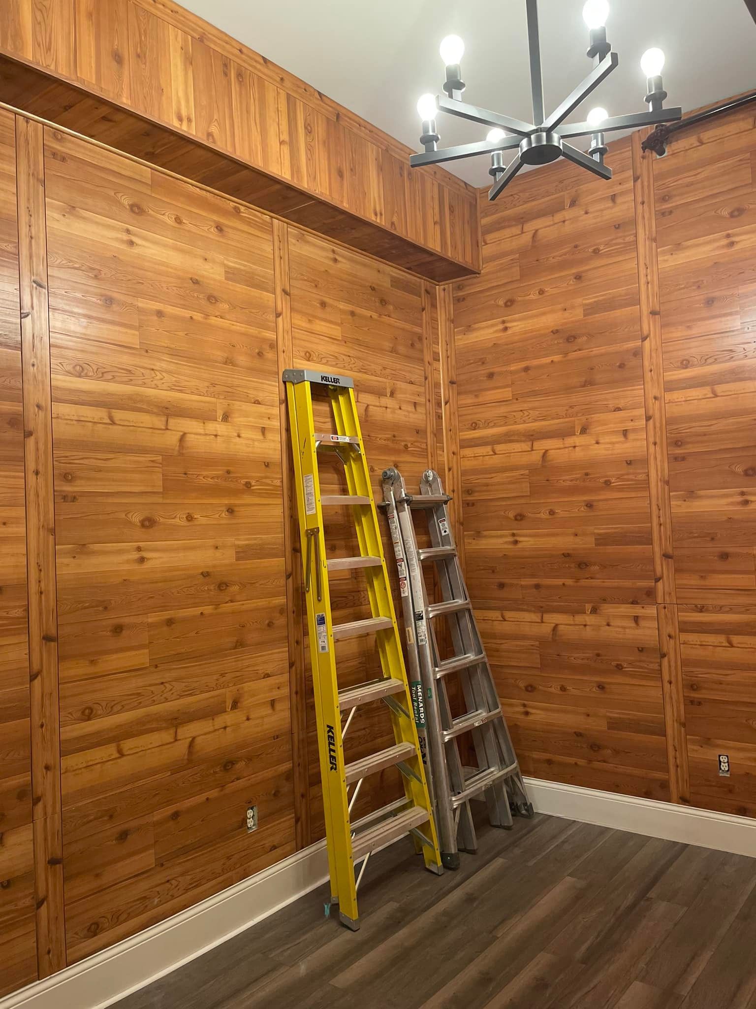Room with wood paneling, two ladders, and a chandelier.