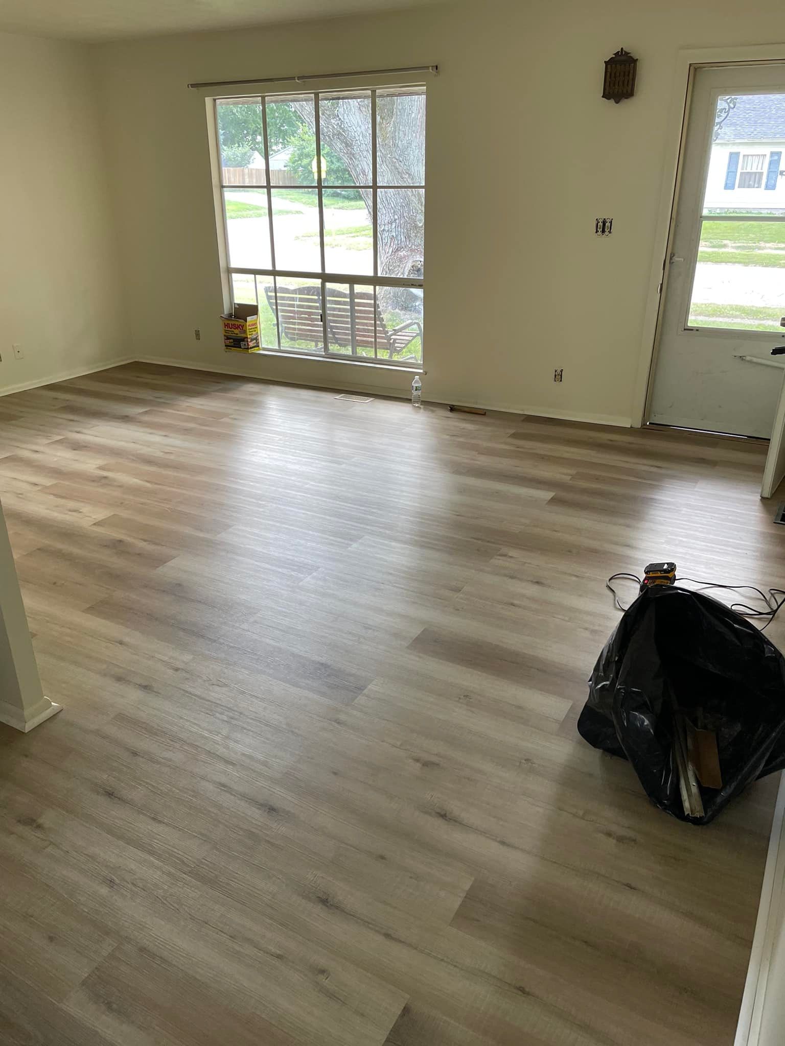 Room with light wood-look flooring, white walls, a window, and a trash bag.