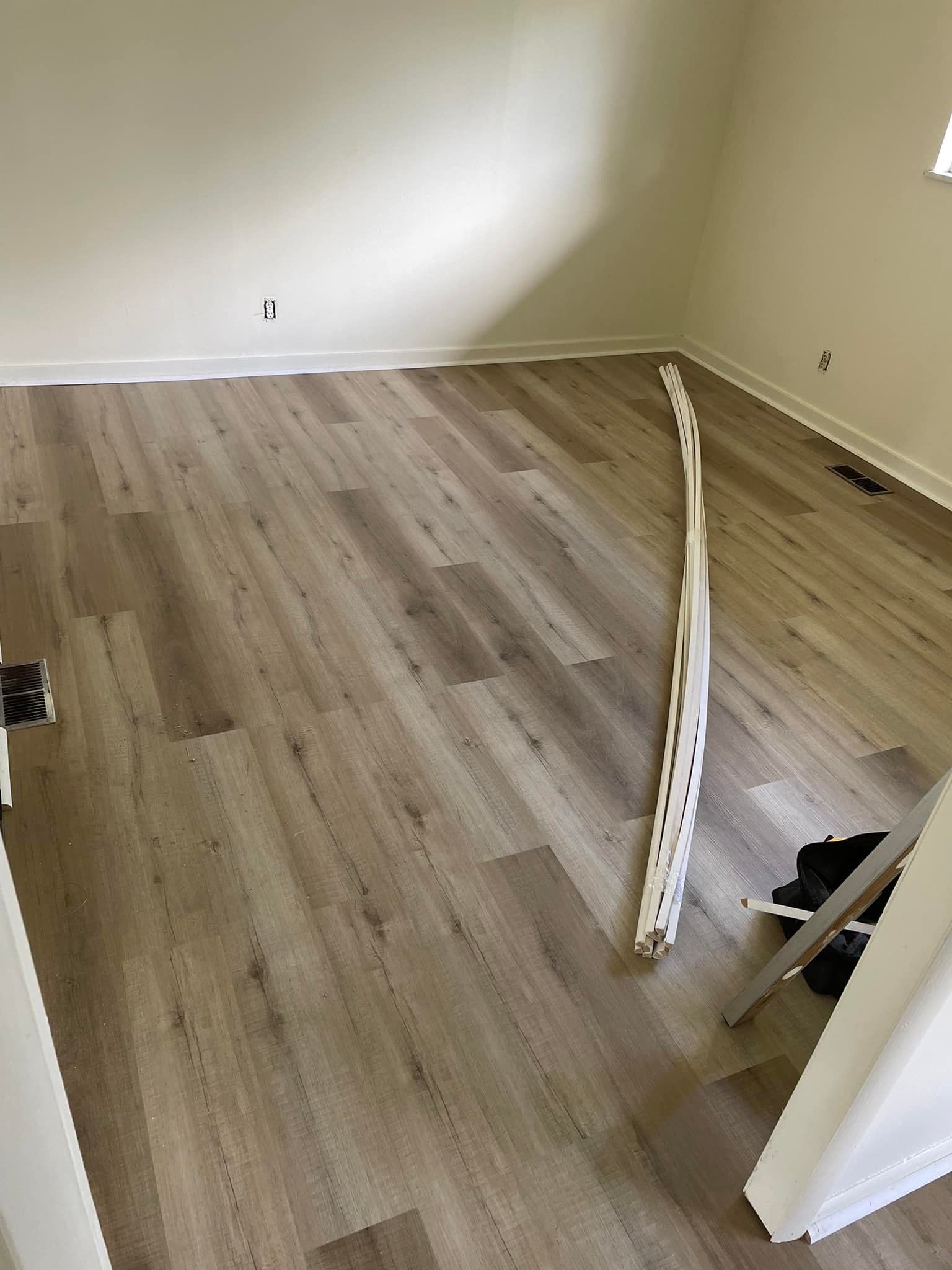 Empty room with light wood-look flooring and white trim. A pile of trim rests on the floor.