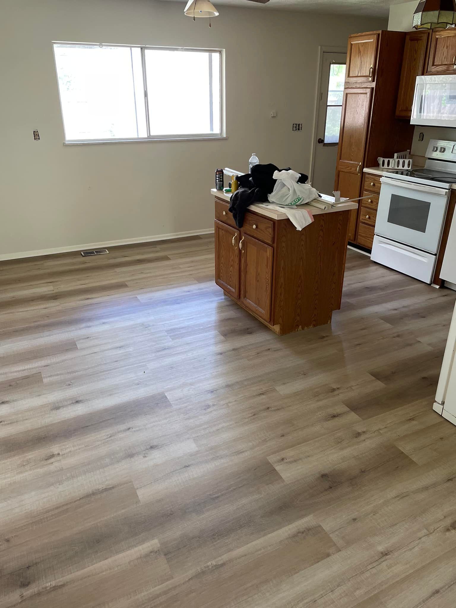 Kitchen with wood-look flooring, a central island, white appliances, and a window.