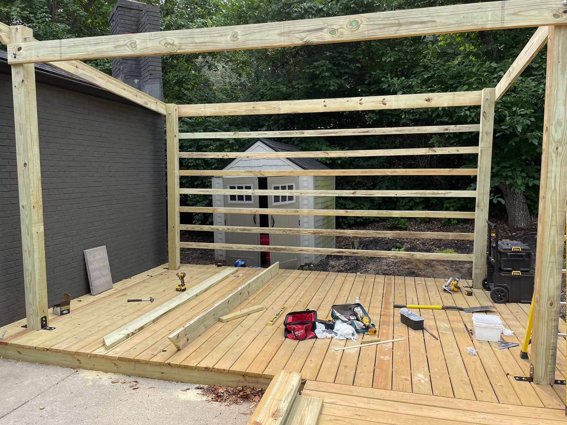 Construction of a wooden deck with a partially built frame; light-colored wood, backyard setting.