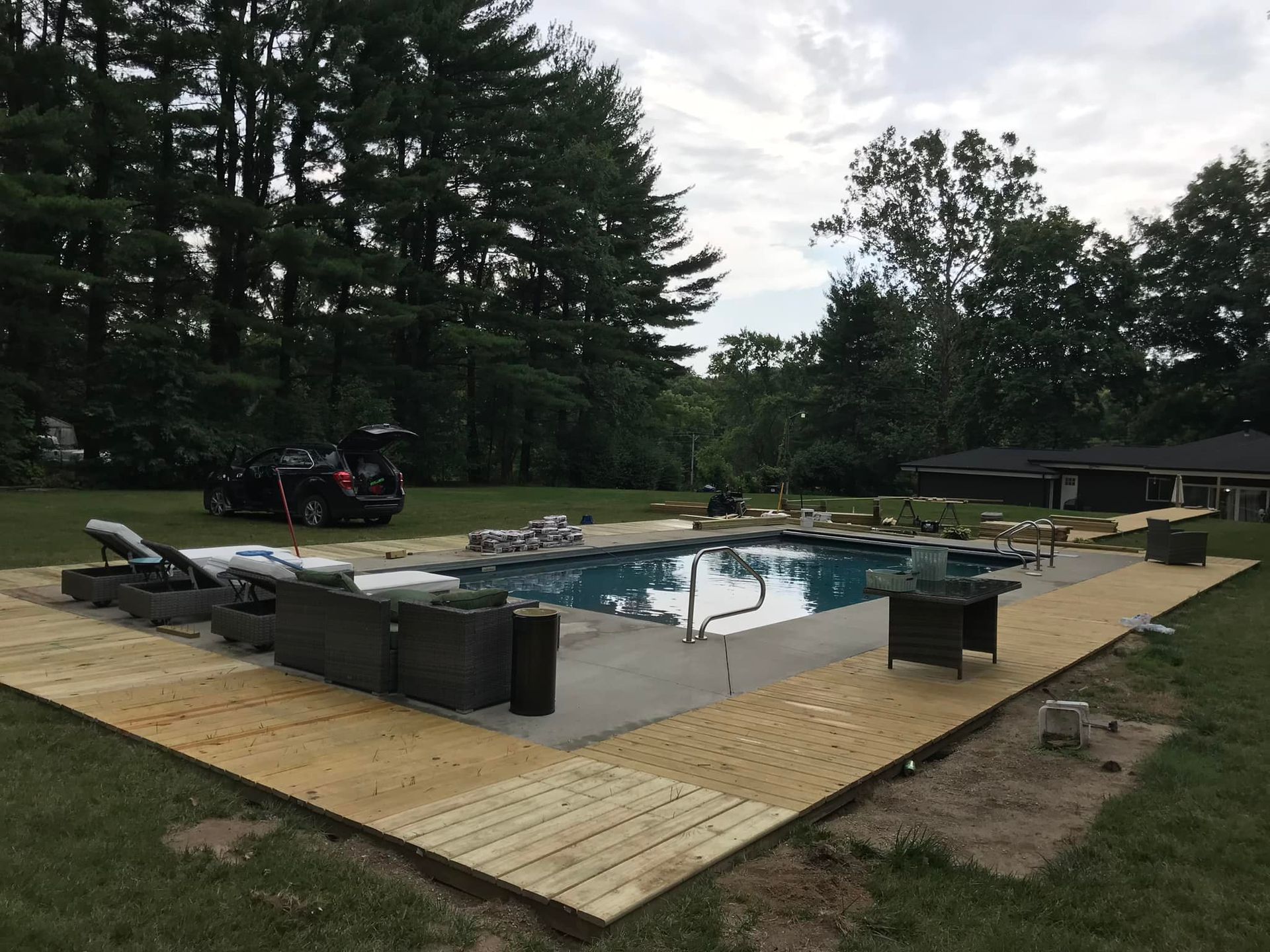 Wooden deck surrounds a rectangular swimming pool; a black SUV sits on the grass.