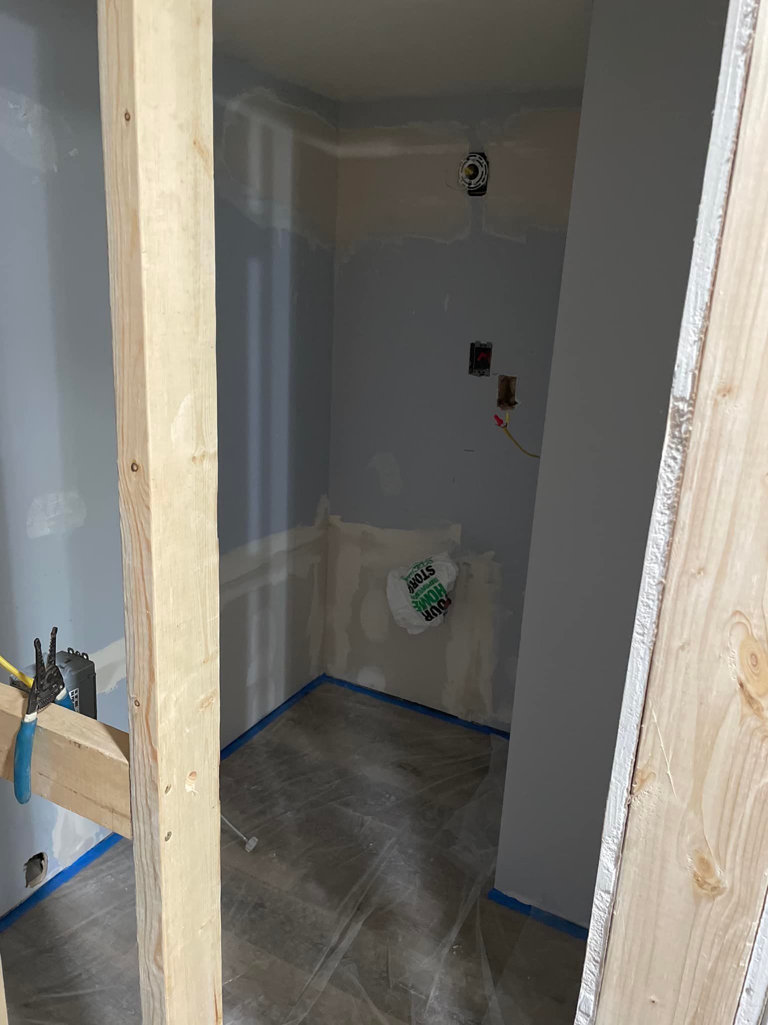Framed bathroom with drywall, electrical outlets, and blue painter's tape. Construction in progress.