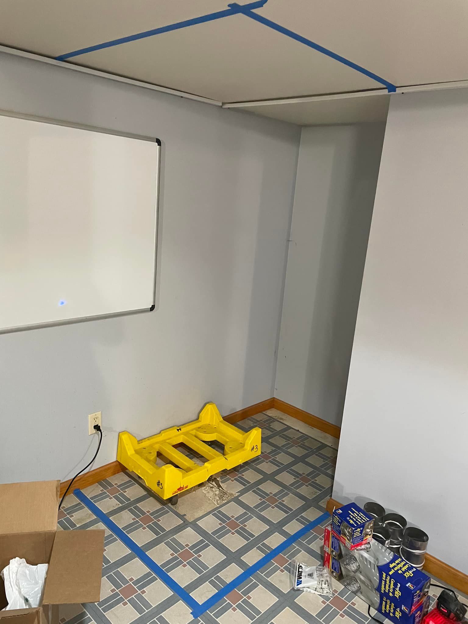 A room with a whiteboard, yellow plastic cart, and patterned floor outlined with blue tape.