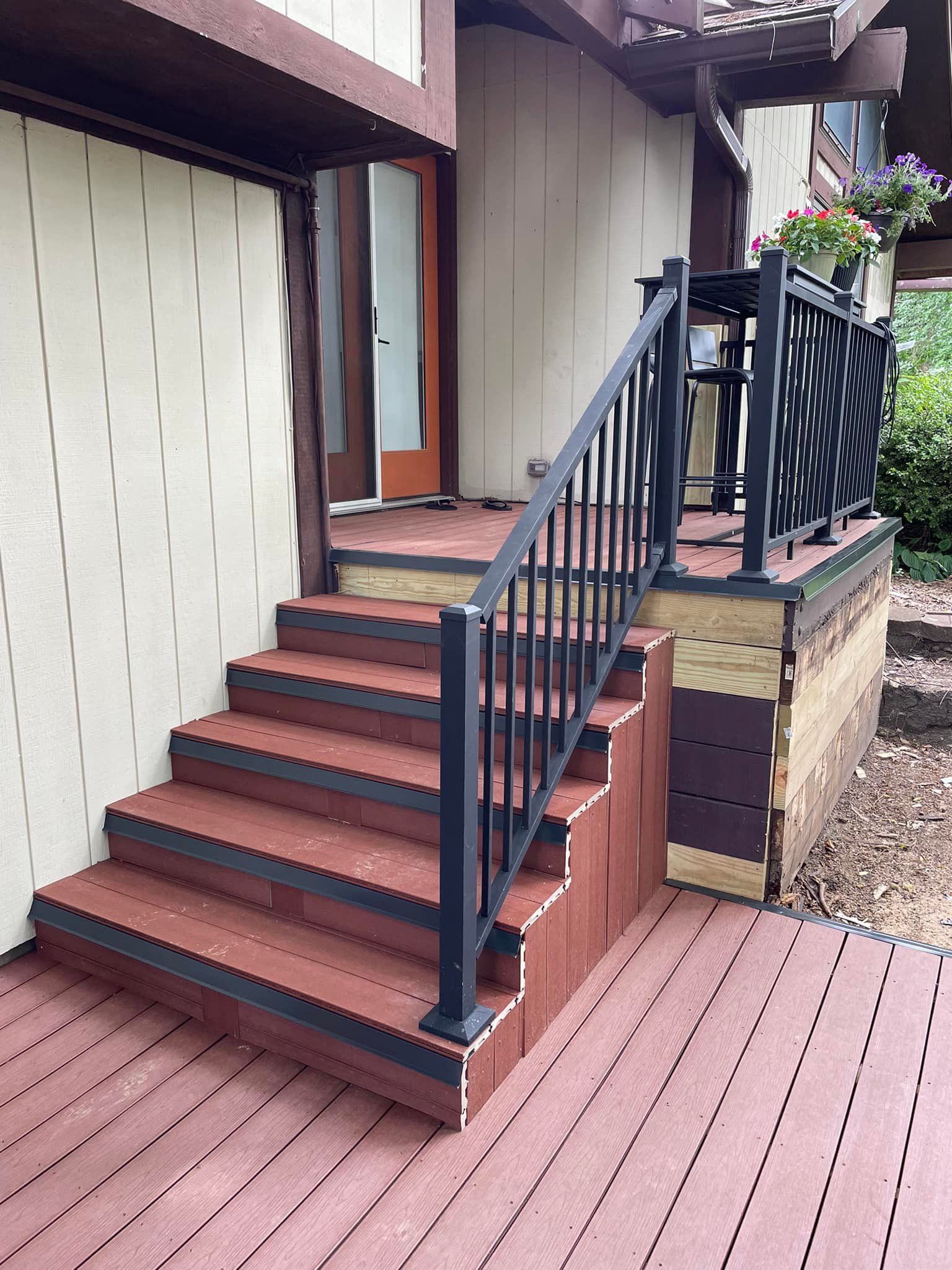 Exterior view: Steps leading to a doorway. Reddish-brown steps and deck, black railing. Beige siding.