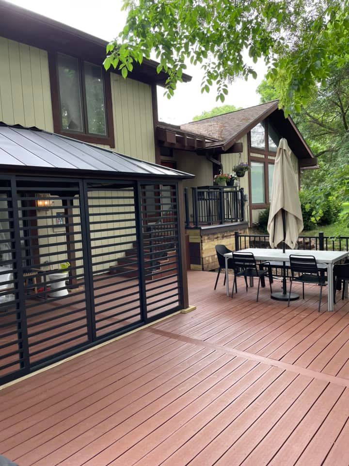 Backyard deck with brown composite decking, dining table, gazebo, and house.