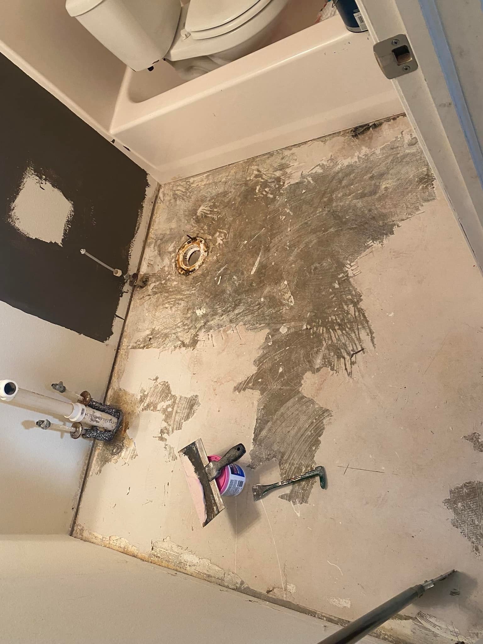Bathroom floor demolition in progress; concrete and old adhesive visible; toilet and plumbing fixtures present.