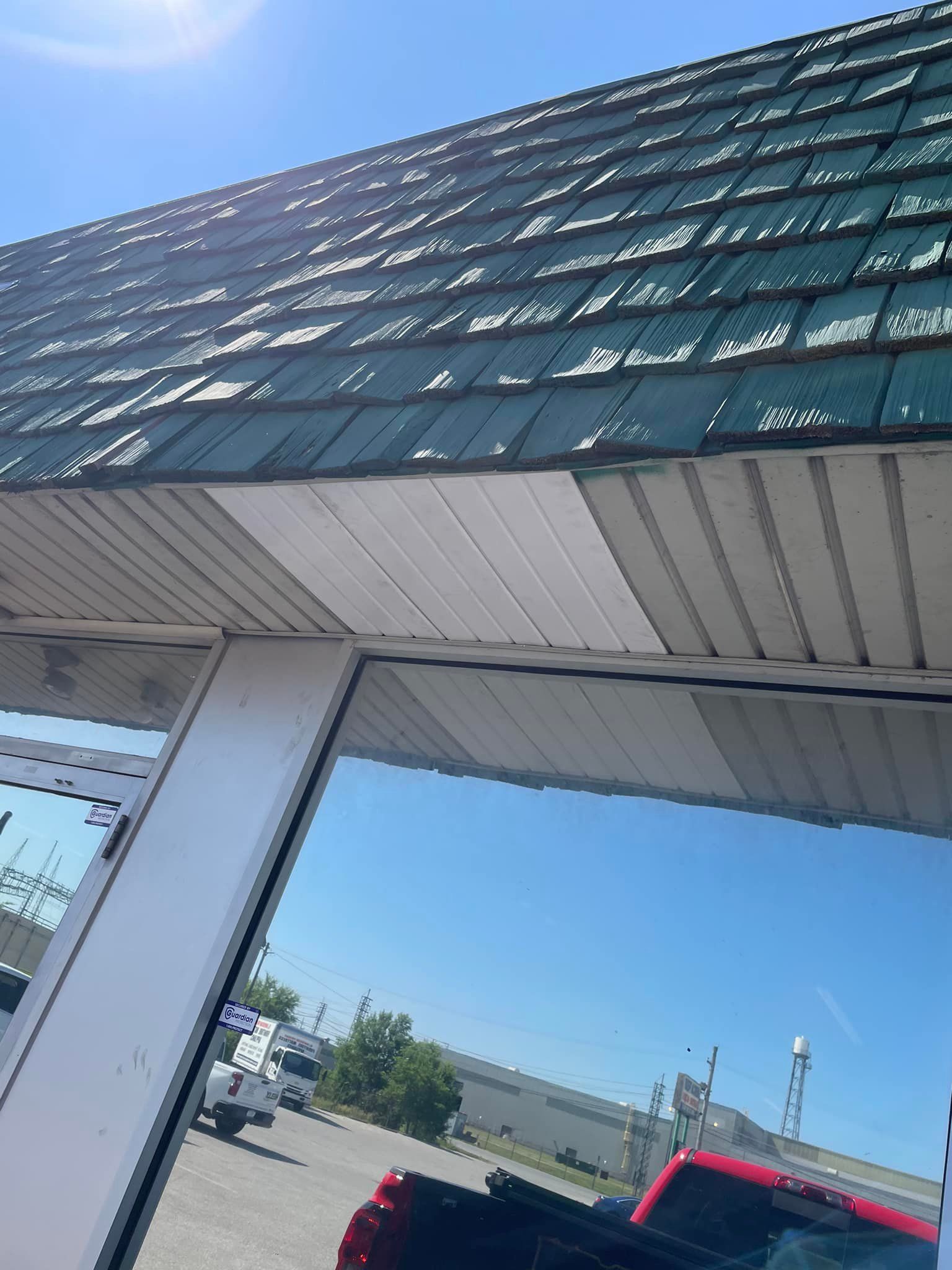 Green roof with white trim over large windows reflecting a blue sky, red truck, and parked vehicles.