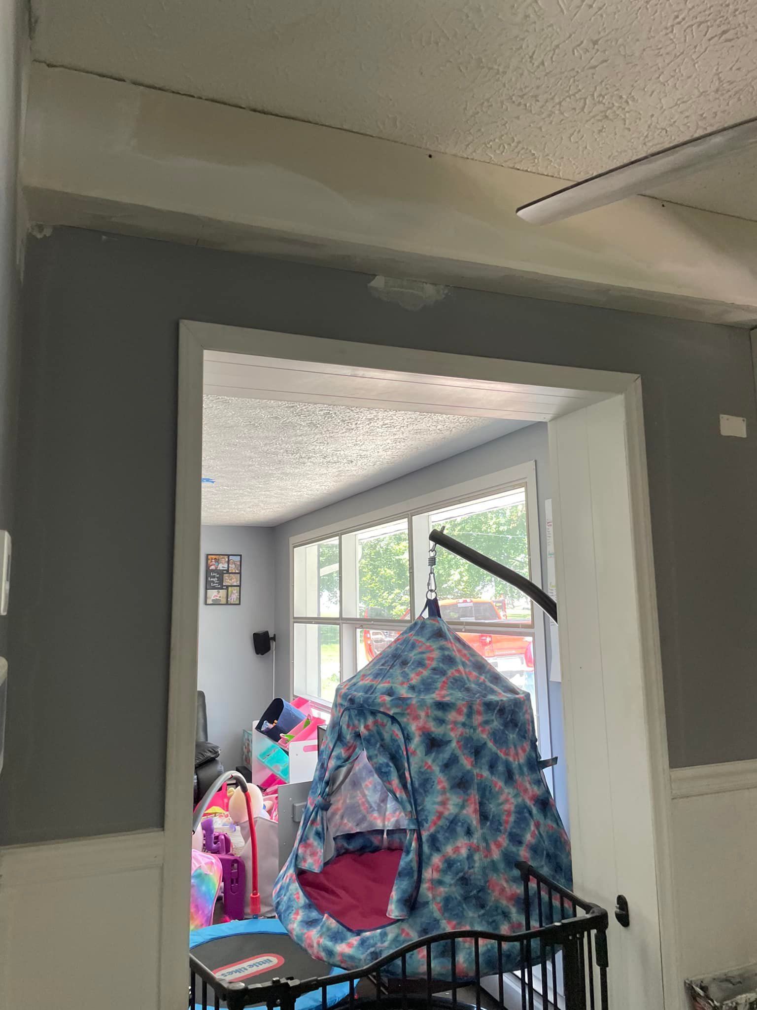 A doorway leads to a room with a swing bed, trampoline, and windows. Gray and white colors are visible.