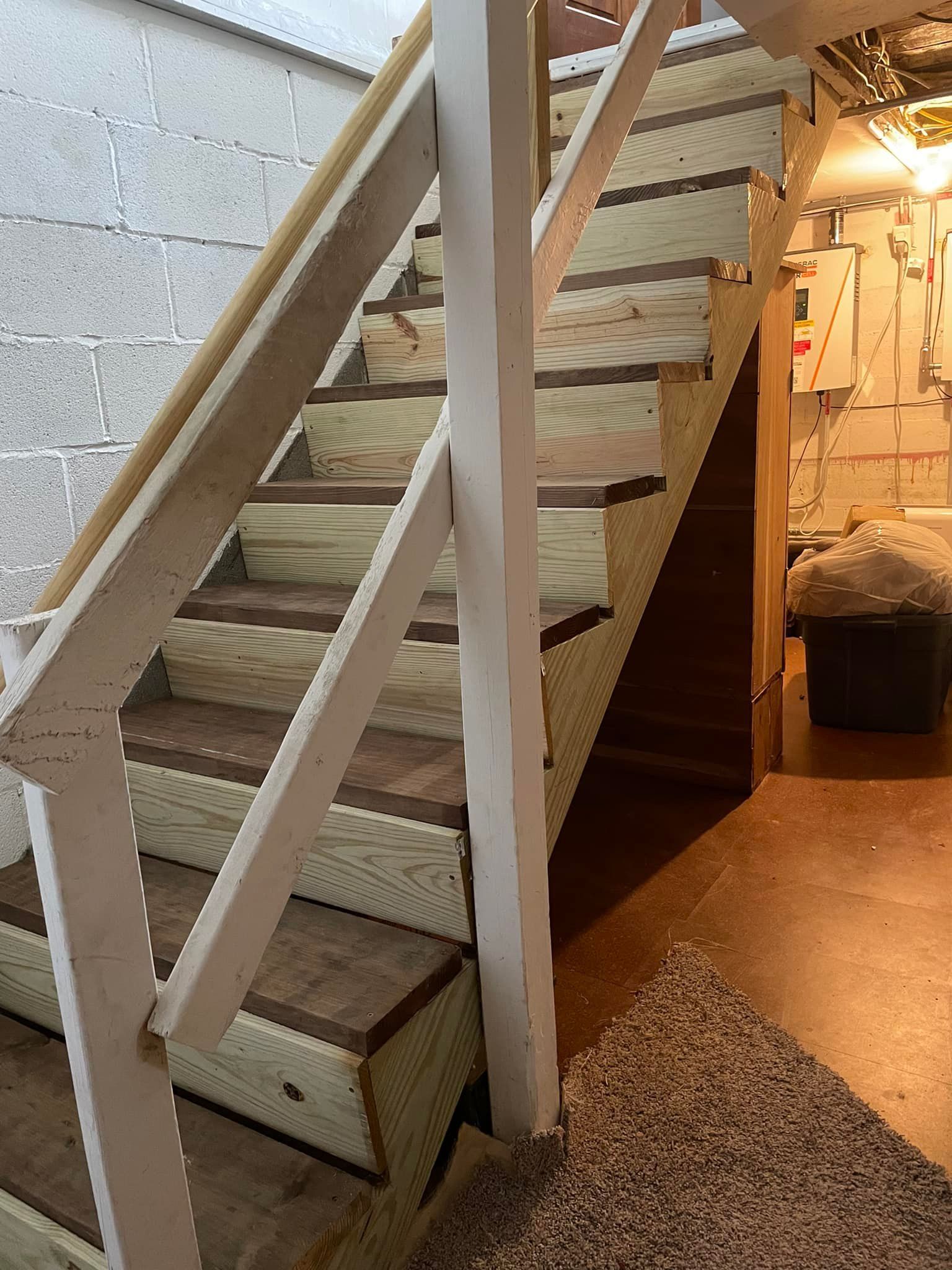 Wooden basement stairs with tan carpet, a white railing, and a brown floor.
