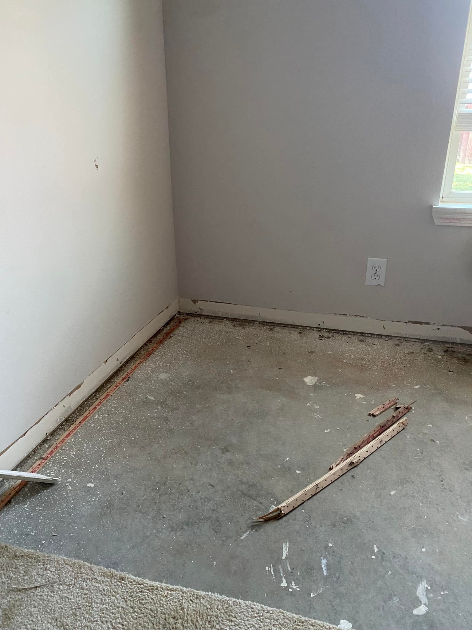 Room with concrete floor, debris and baseboard removed, walls are white and gray, window in the corner.