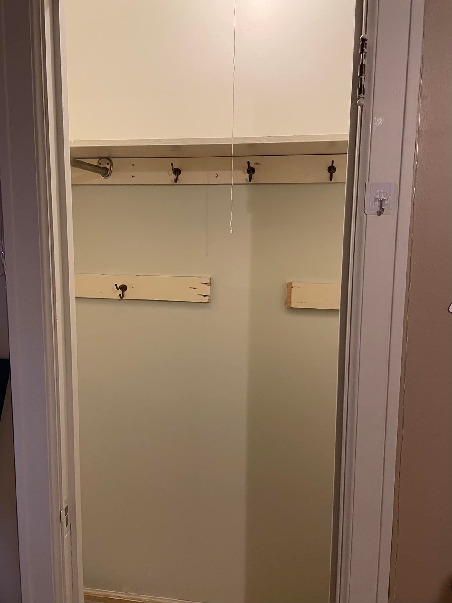 Empty closet with beige walls and wooden shelves with hooks.