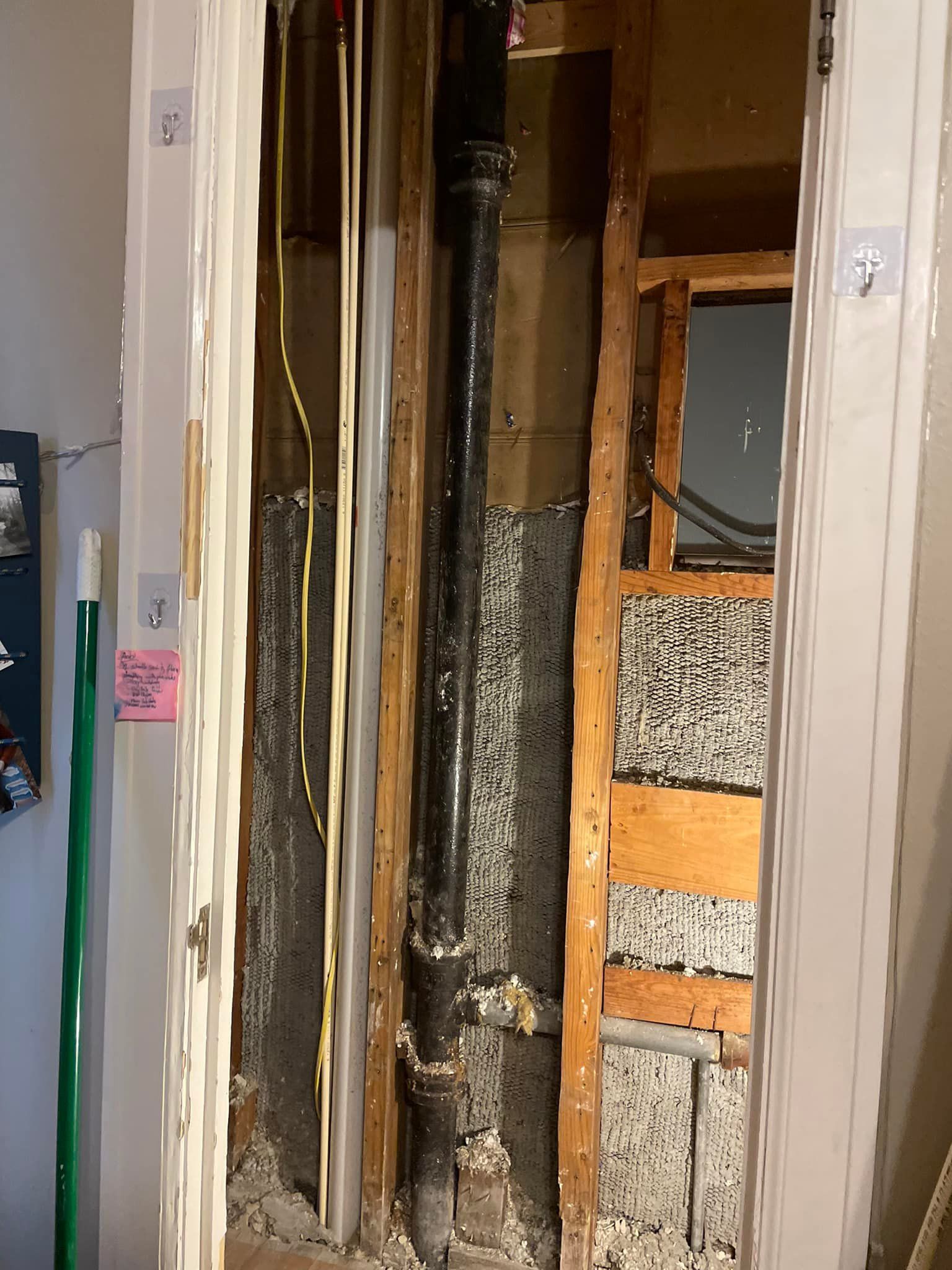 Exposed interior wall with black pipe, wires, and wood framing, possibly during construction or repair.