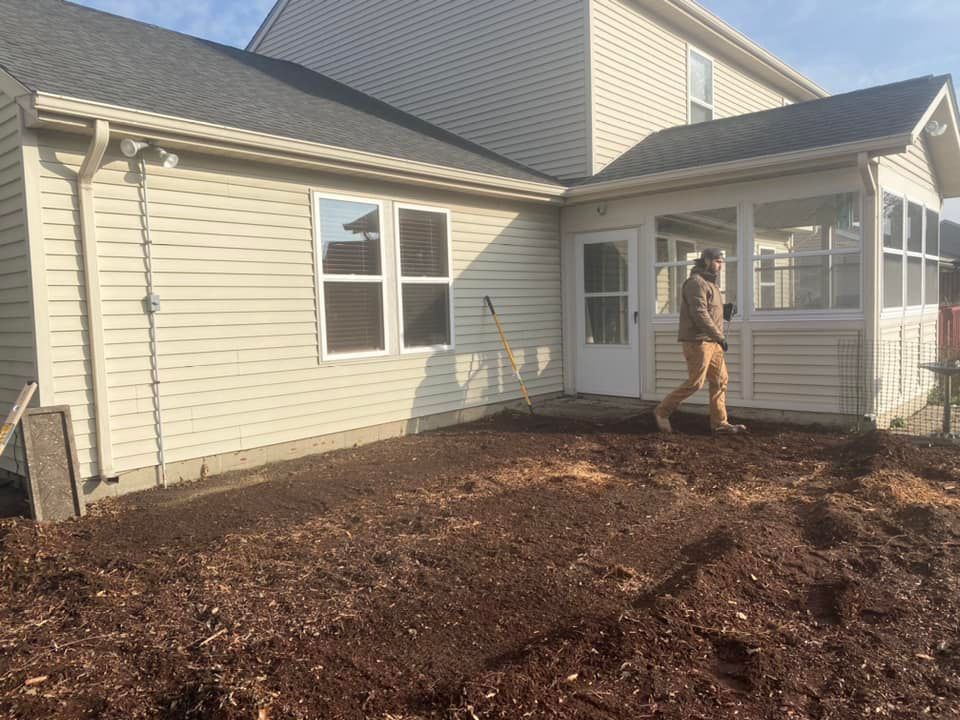 A person walks on dark mulch in front of a house with a sunroom.