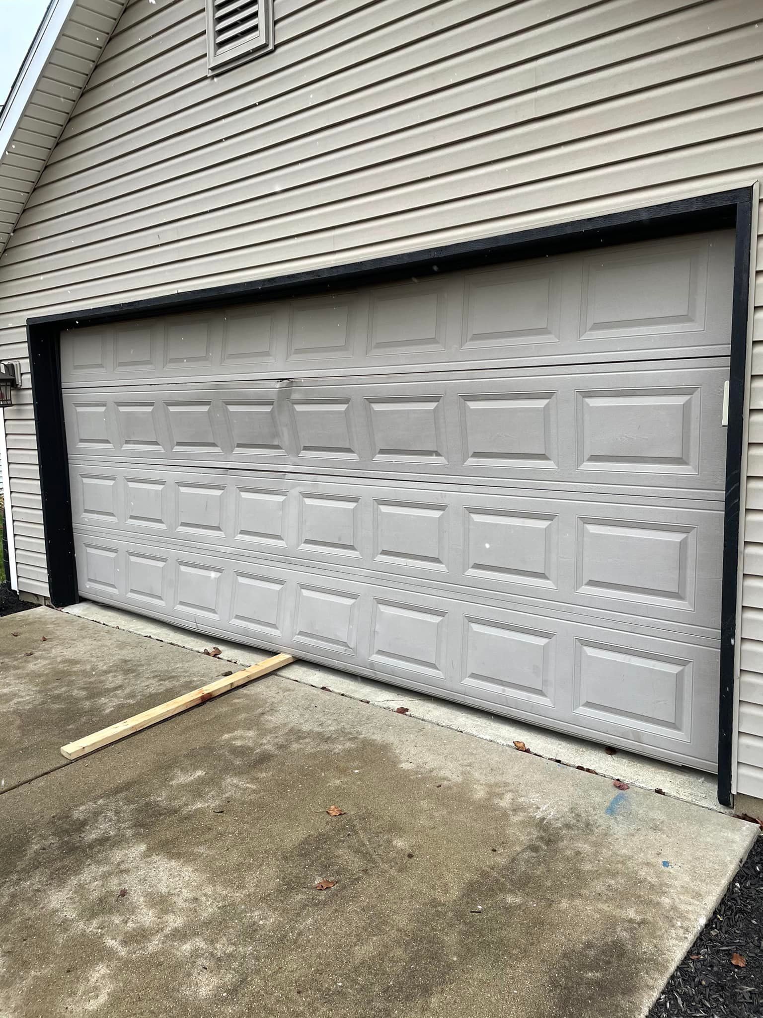Gray garage door with black trim on a house with gray siding; concrete driveway.
