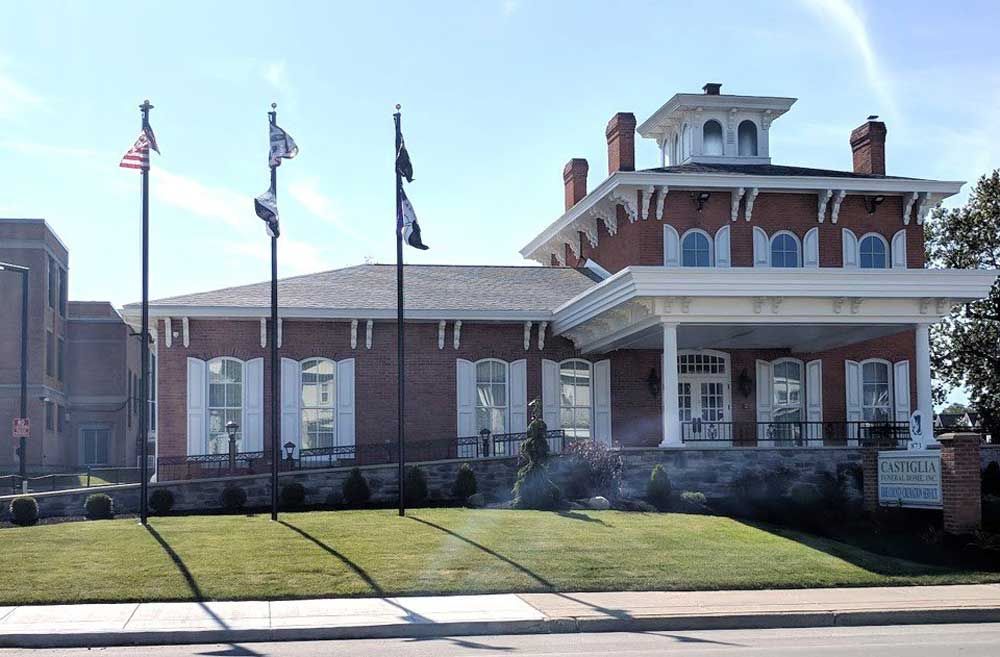 A brick building with white trim, a cupola, and three flagpoles on a green lawn under a clear blue sky.