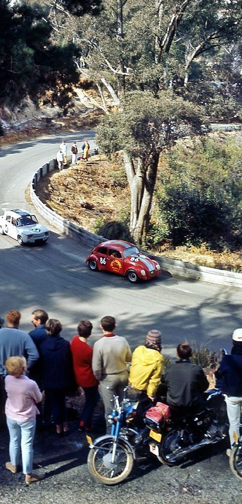 A group of people are watching a car race on a curvy road.